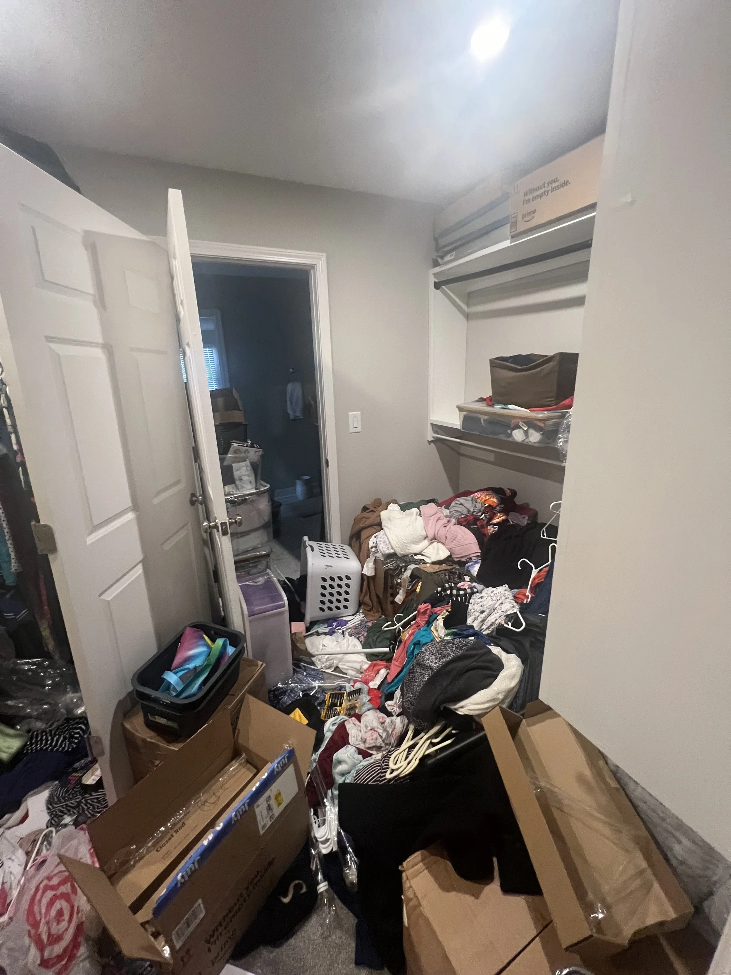 A cluttered room with clothes, shoes, boxes, and miscellaneous items scattered on the floor and shelves.