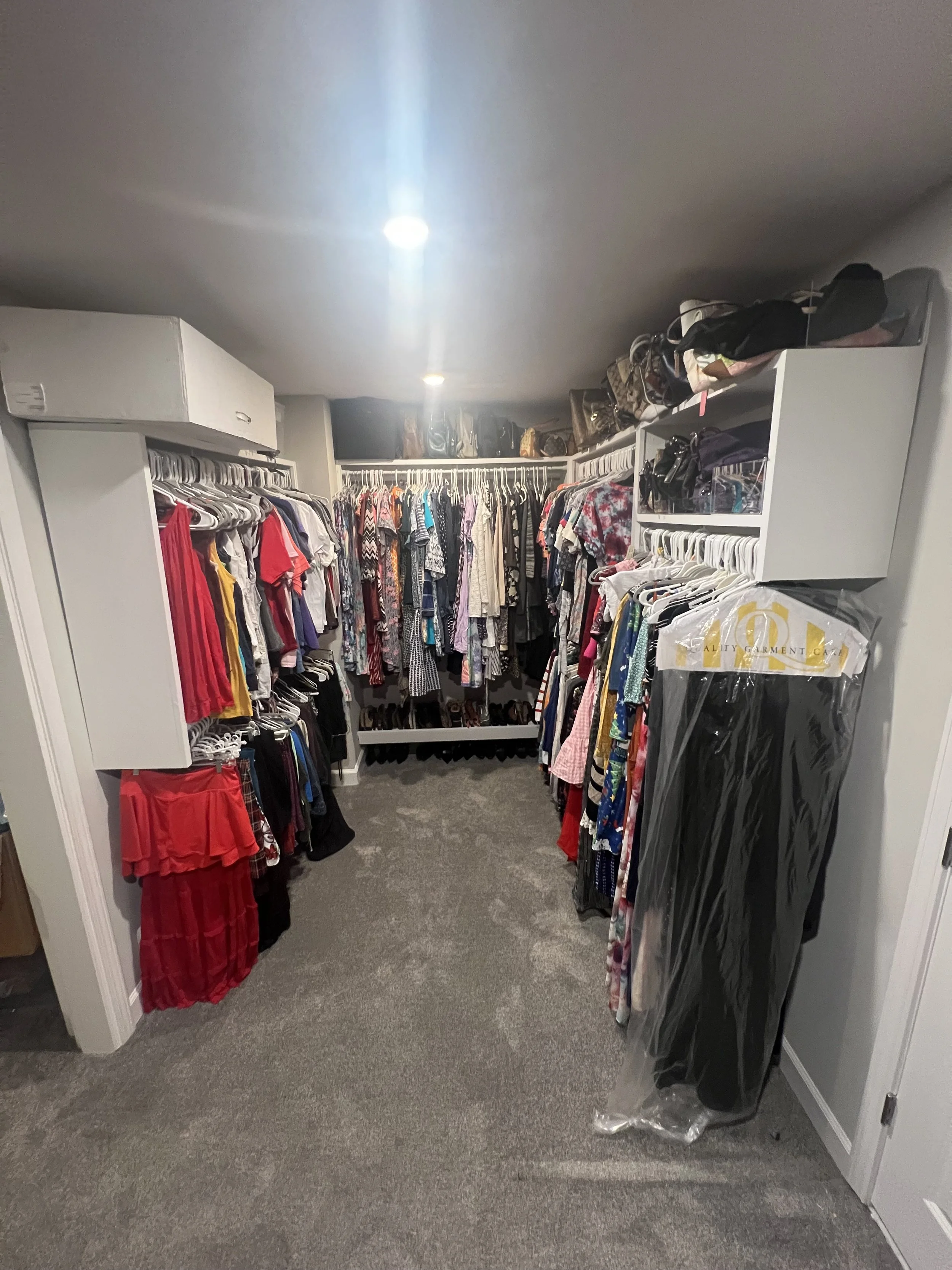 A walk-in closet filled with clothes on racks, shoes on the back wall, and storage shelves on either side.