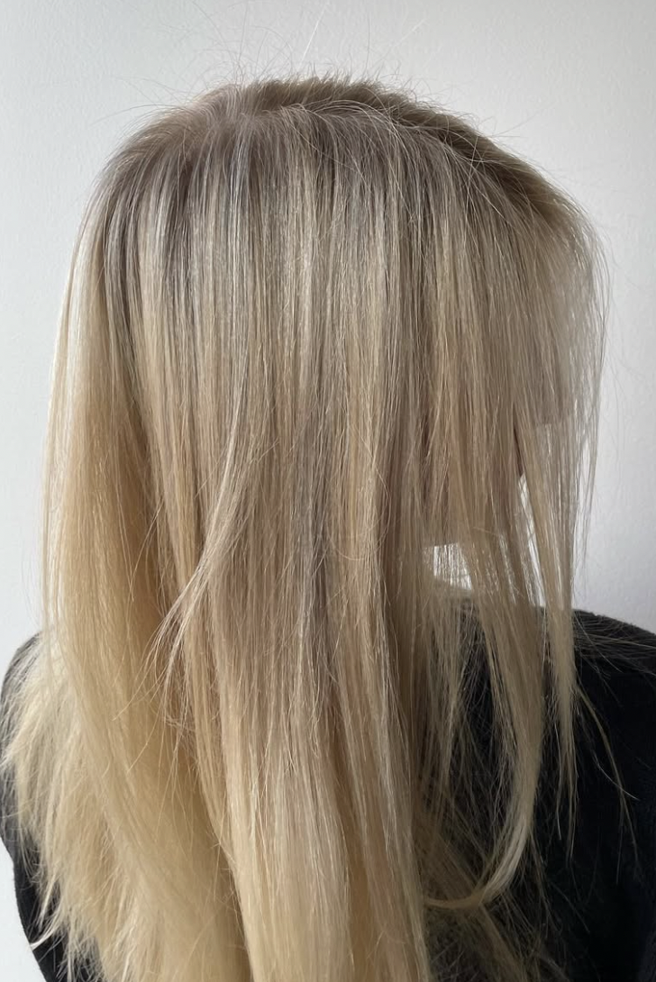 Blonde hair with darker roots and some loose strands, viewed from the side against a plain light background.