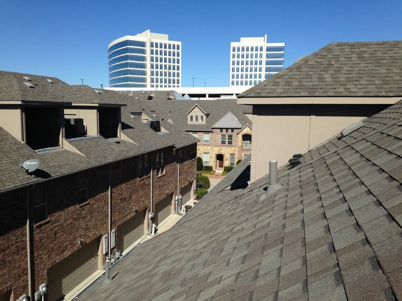 View of rooftops of residential buildings with two tall modern office buildings in the background, clear blue sky.