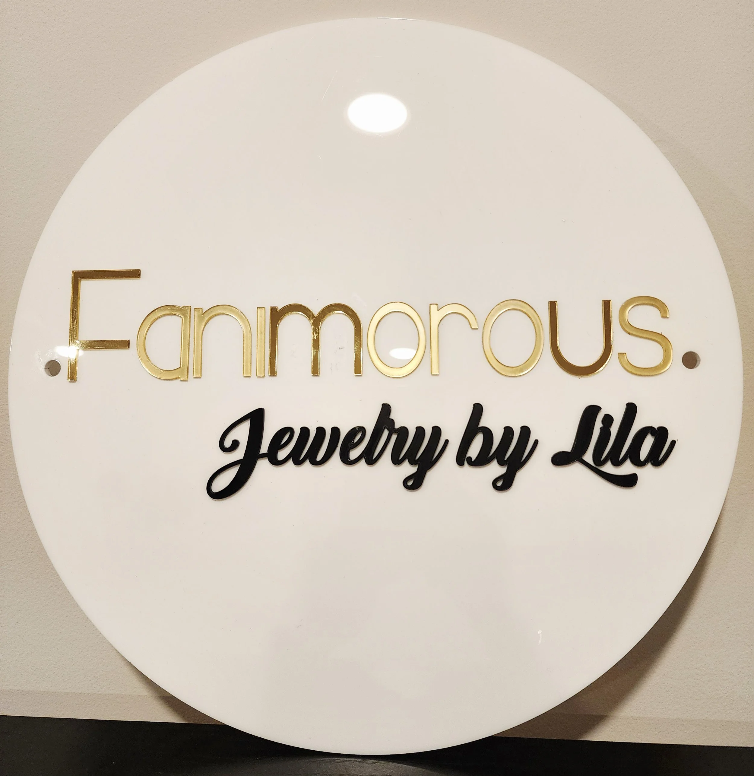 Circular sign with the text "Farnmarous Jewelry by Lila" in gold and black lettering.