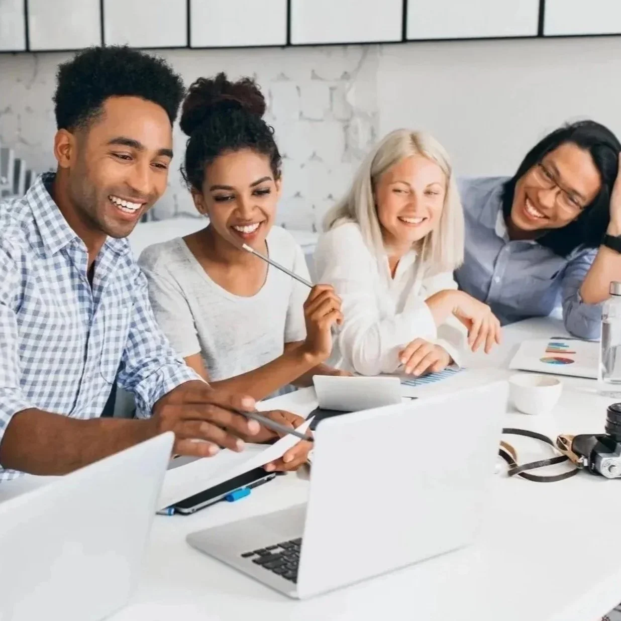 Group of diverse professionals working and collaborating at a modern office meeting table, smiling and discussing ideas.