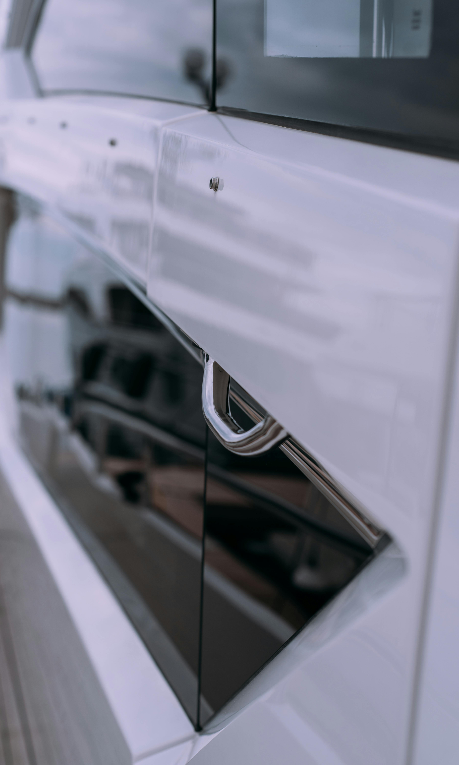 Close-up of a modern white car's side door with a chrome door handle.
