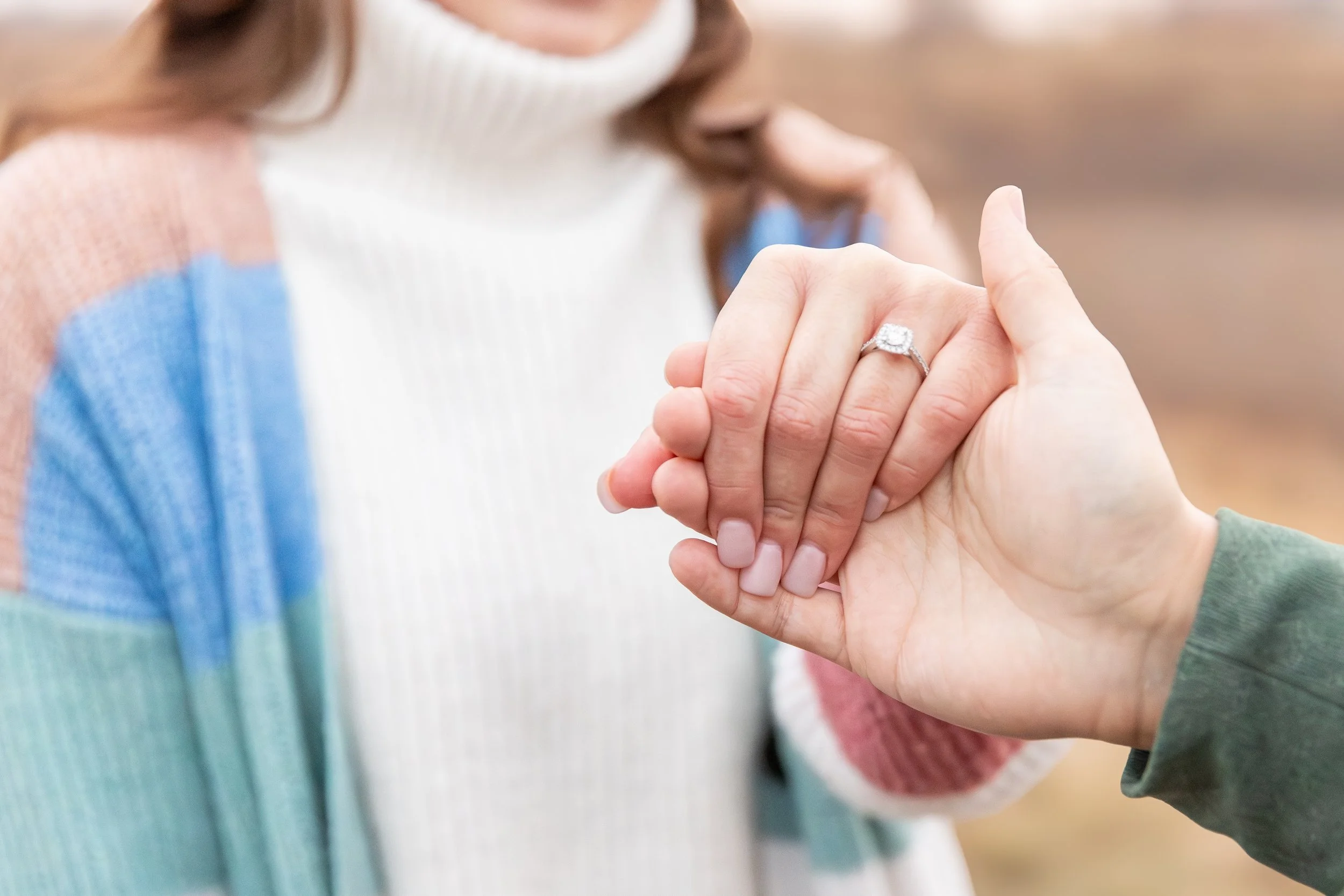 Close-up of a woman showing her engagement ring as she holds hands with another person.