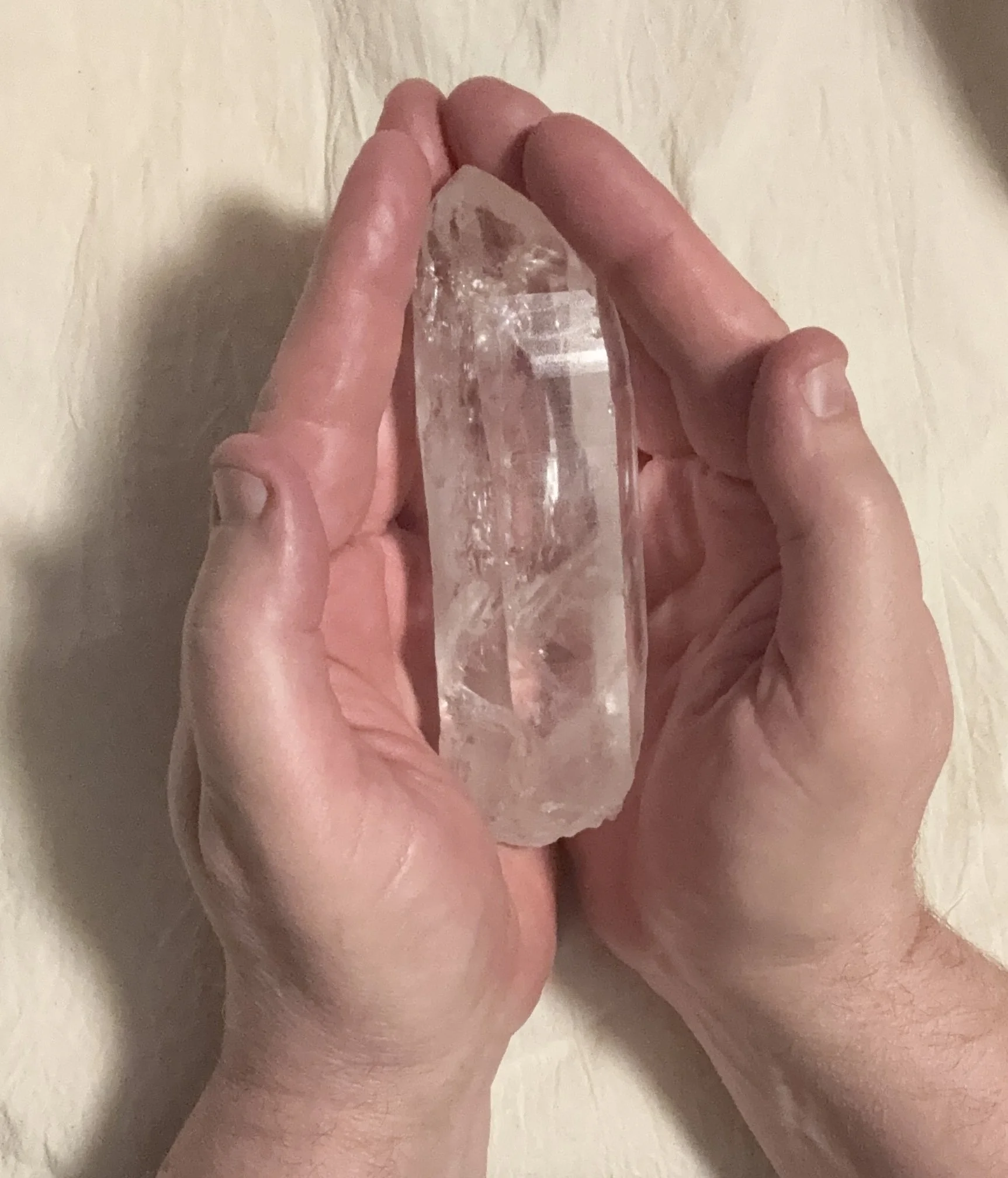 A person holding a large, clear quartz crystal in their hand with a neutral background.