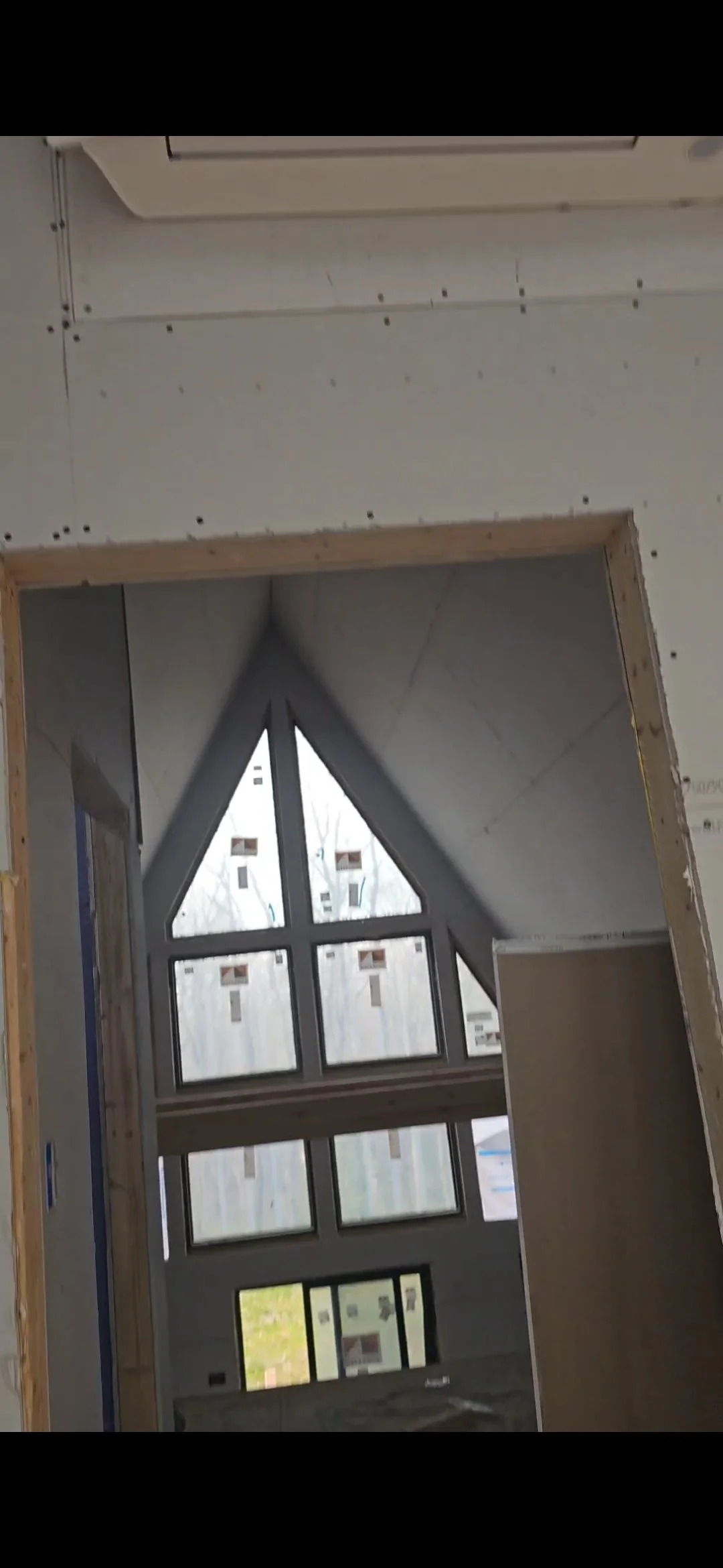 Interiores de una construcción en progreso con ventanas y paredes en proceso de acabado, incluyendo un techo inclinado con ventanas y ensamblajes de drywall.