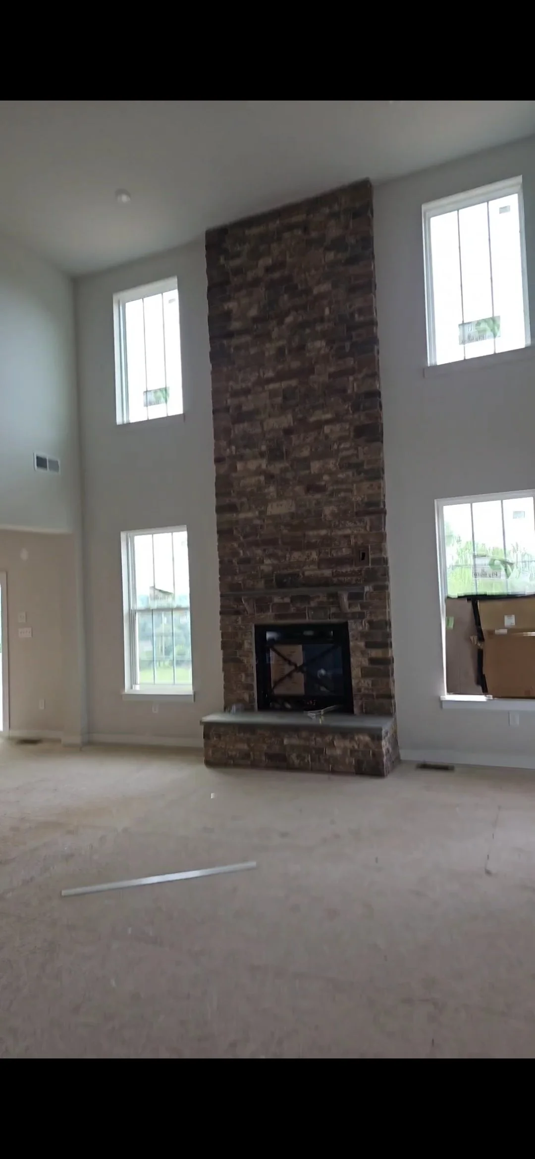 Sala de estar con chimenea de ladrillo y ventanas altas en paredes blancas.