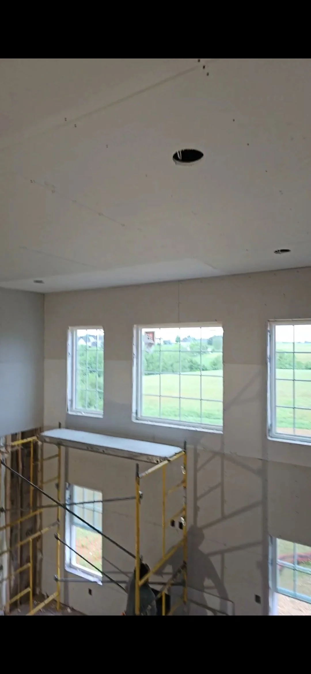 Interior en construcción con ventanas grandes, andamios y tareas de trabajo en proceso.