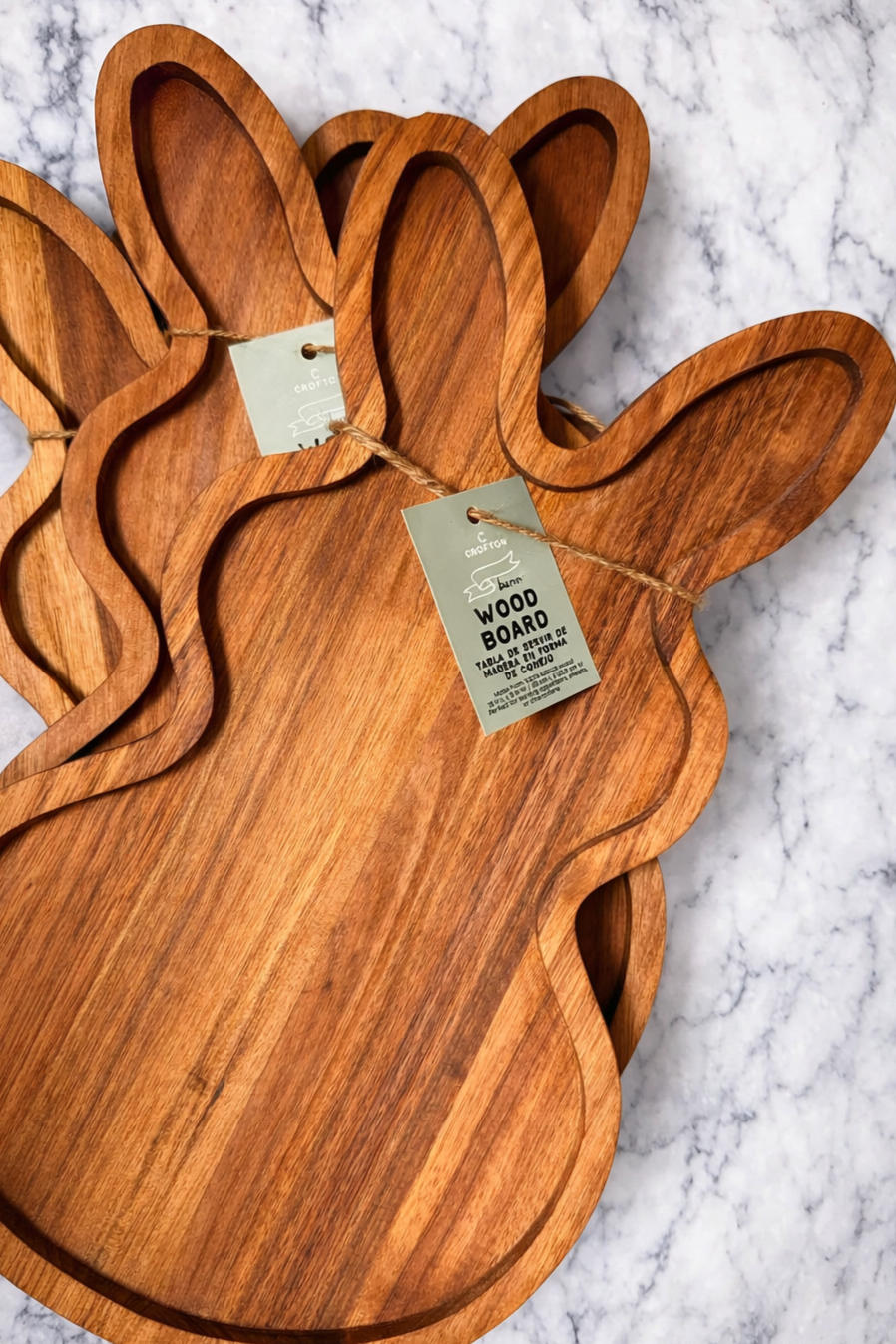 Wooden cutting board shaped like a rabbit with a tag indicating it is made of wood, resting on a marble surface.