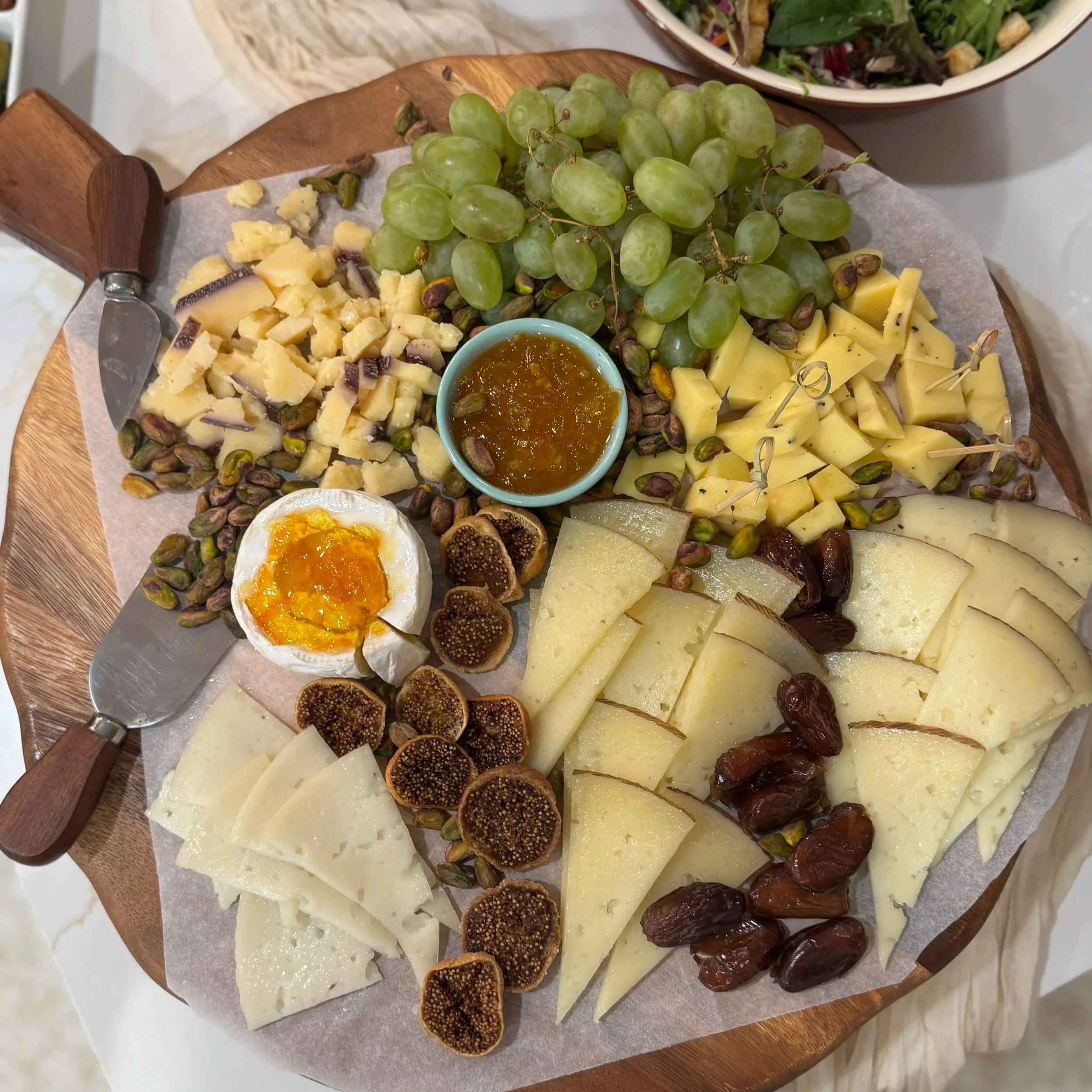Cheese platter with grapes, dried figs, honey, and nuts, served on a round wooden board.