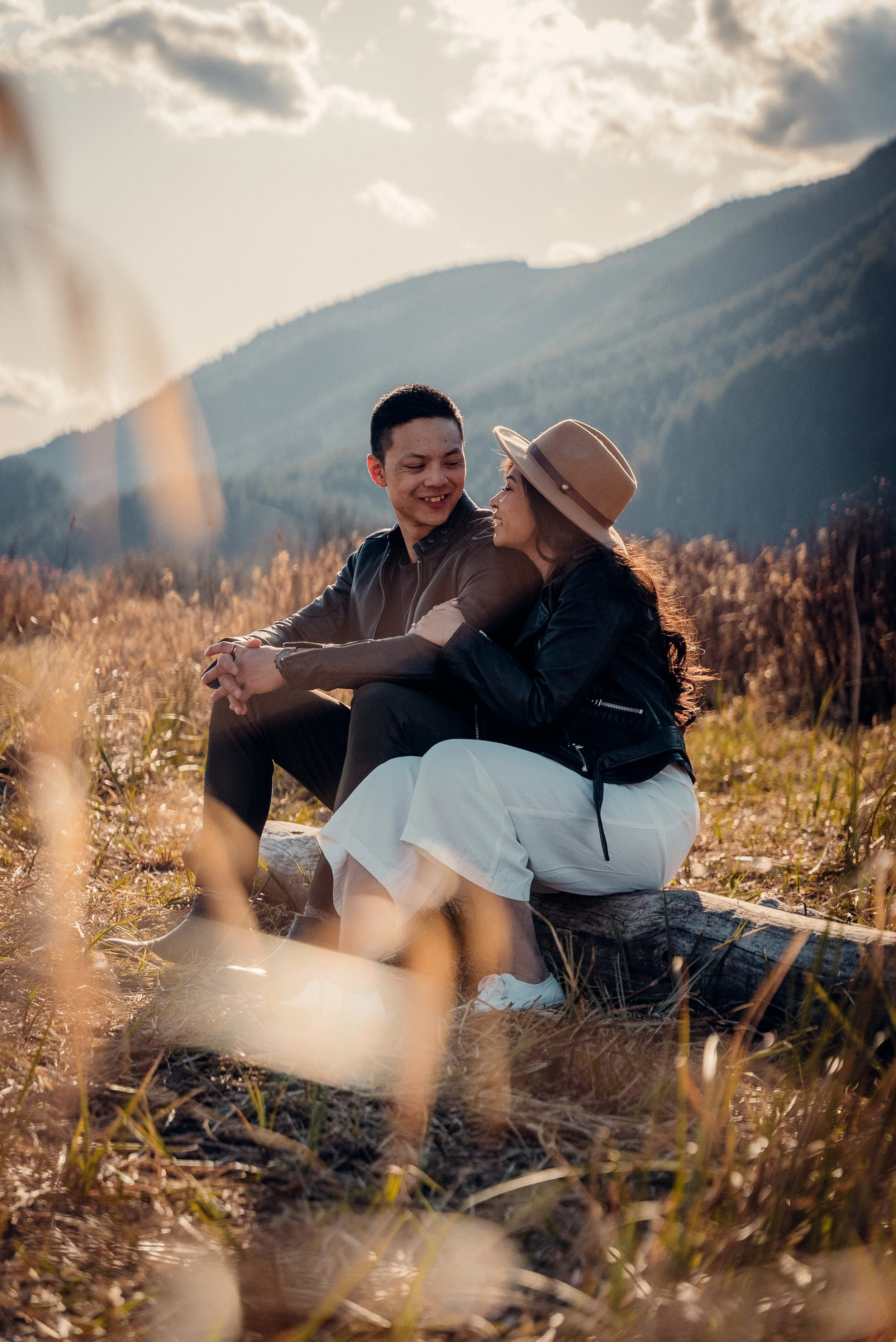 Asian couple sitting in tall grass during their engagement shoot at Pitt Lake, Vancouver