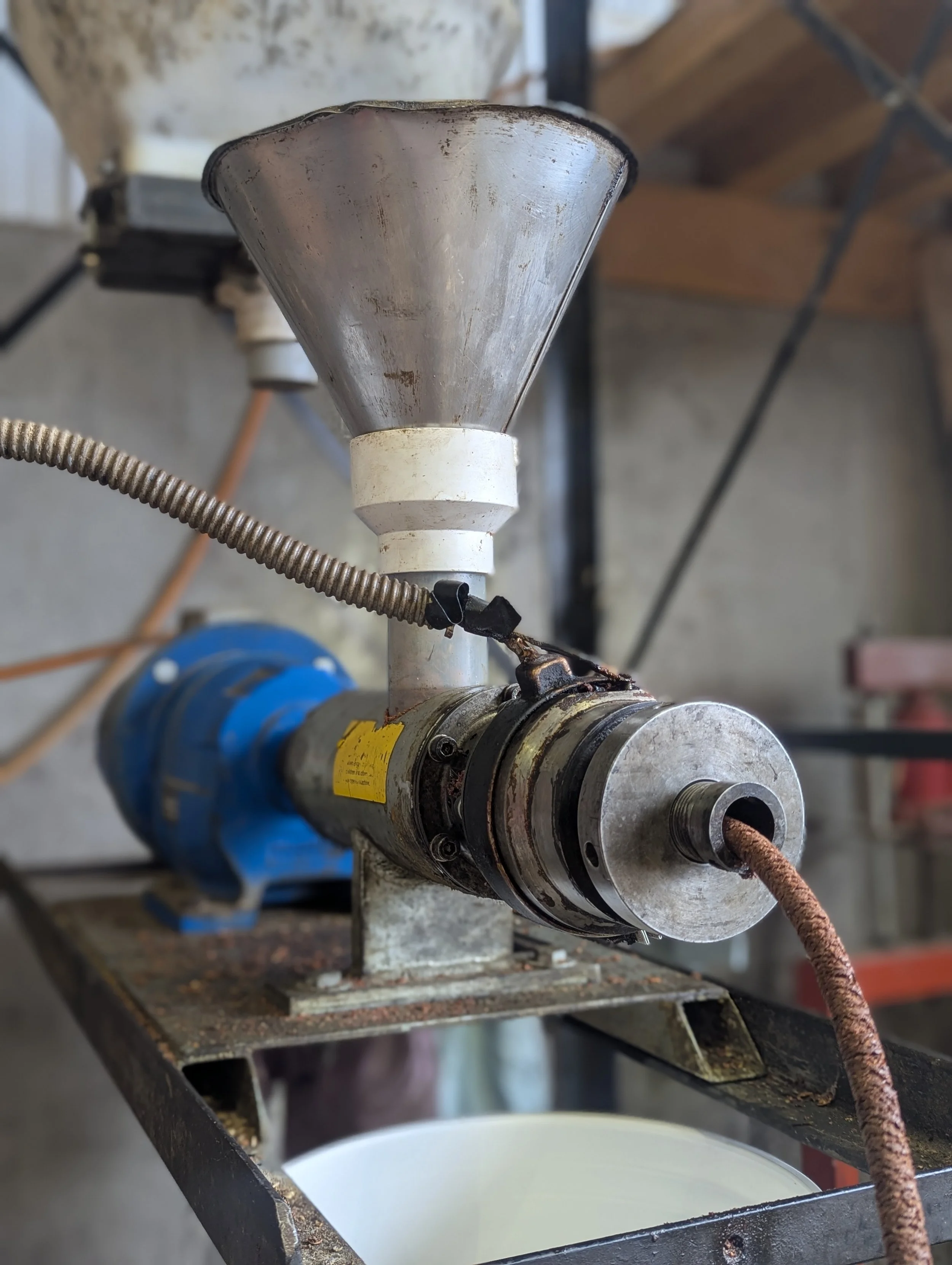 Industrial machine with a funnel, metal components, and a rusted electrical cord, set on a metal stand in a workshop.