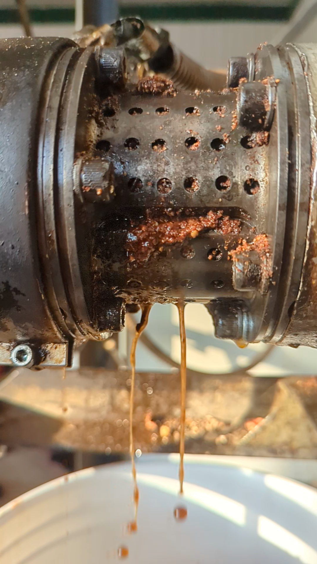 Close-up of a rusty mechanical device with brown liquid dripping from it into a white container.