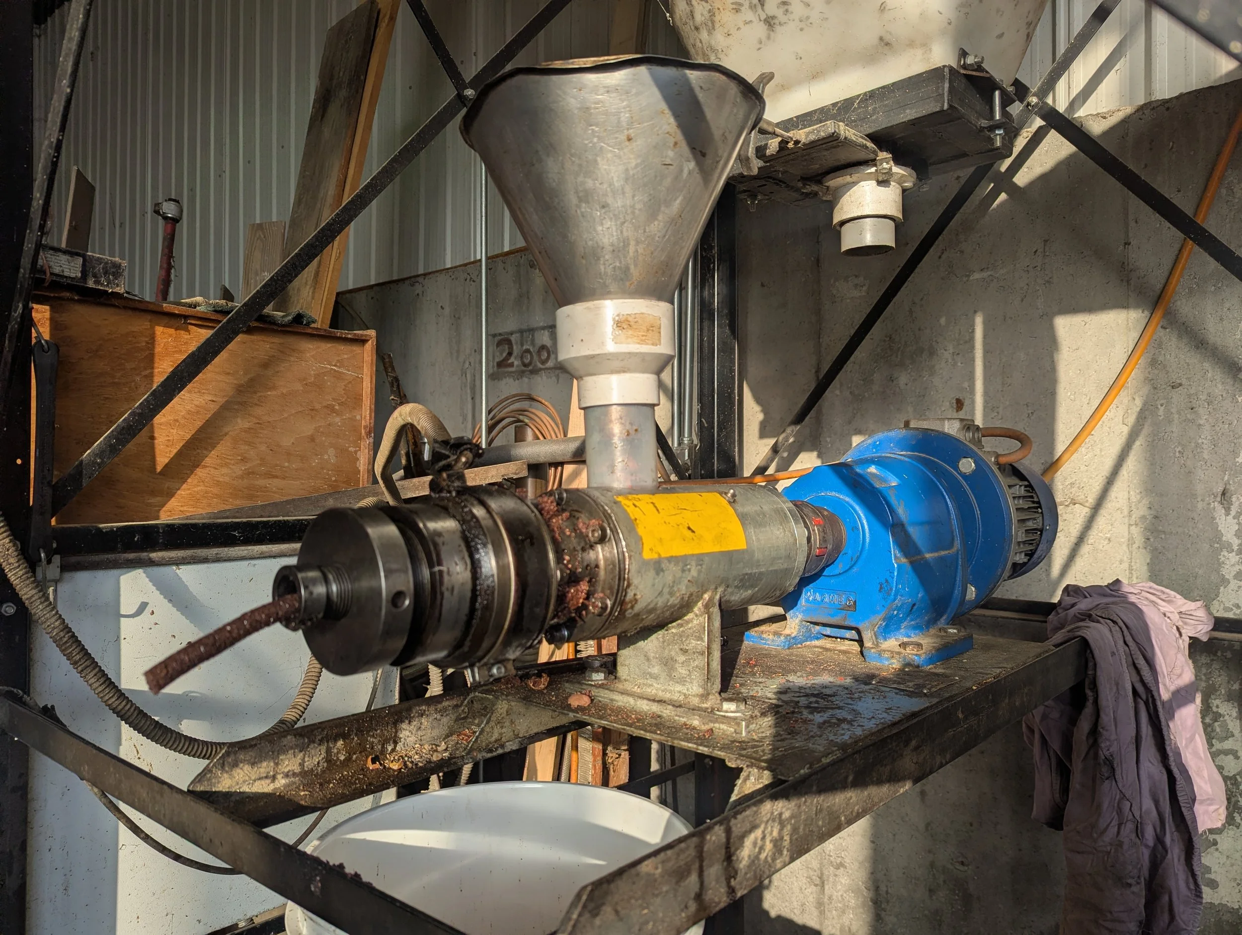 Industrial machine with large metal funnel, motor, and rusty components on a metal frame in a workshop.