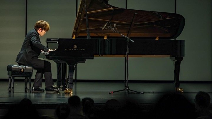 Young boy Hao Rao playing grand piano on stage during performance.