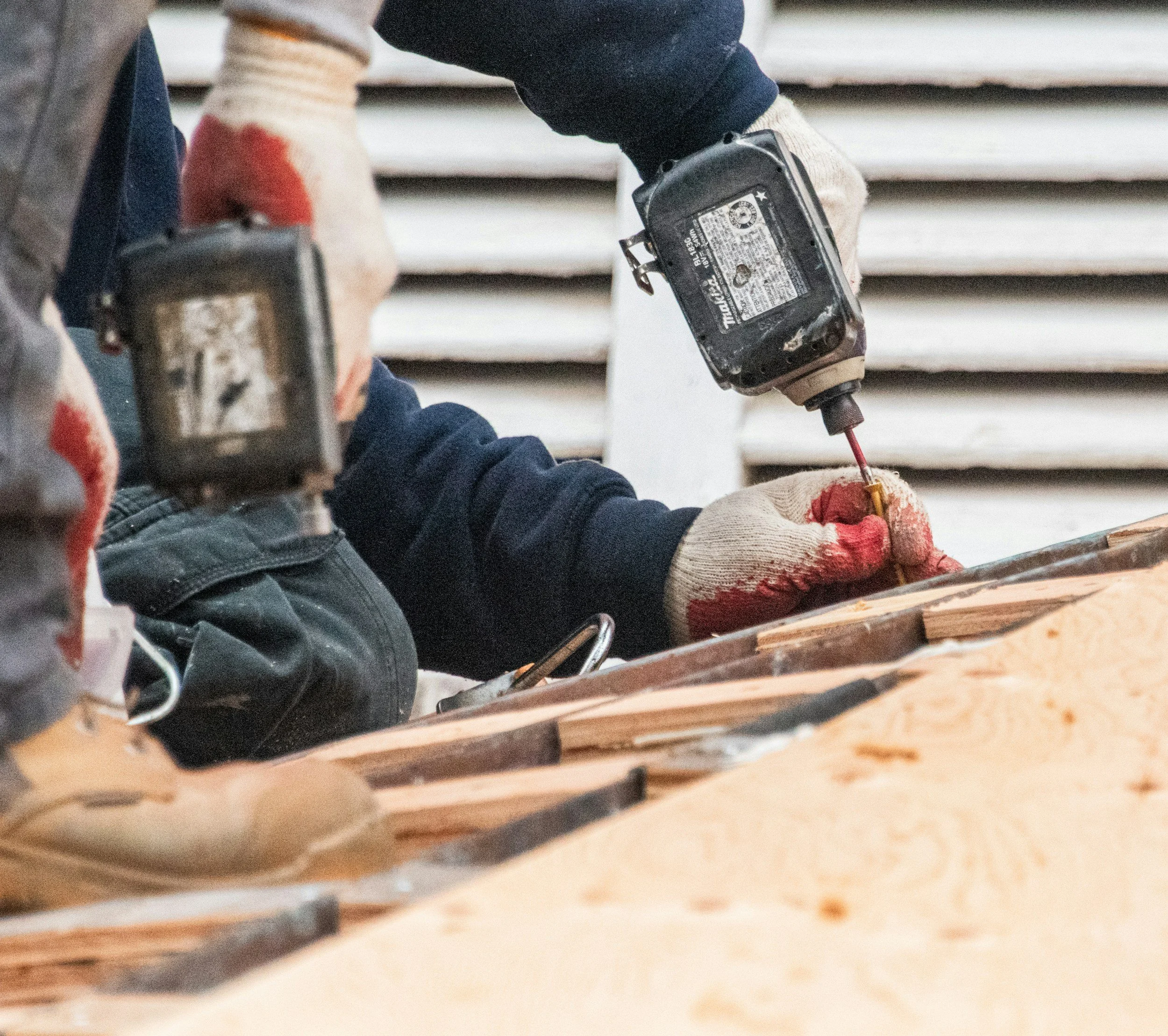 Close-up of a construction worker using a power drill on wooden planks, wearing work gloves.