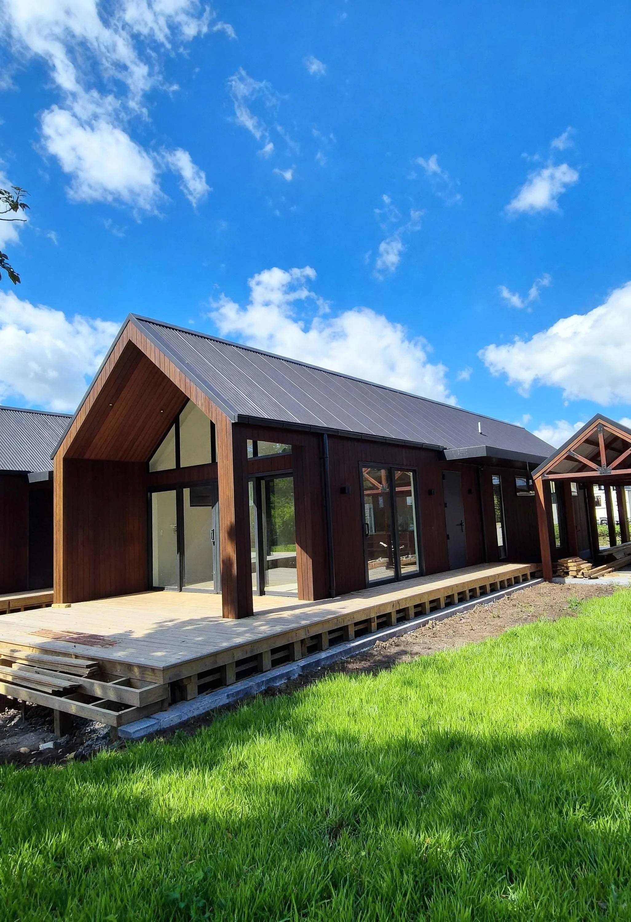 Newly built modern house with wooden exterior, large glass windows and doors, under construction on a sunny day with blue sky and clouds