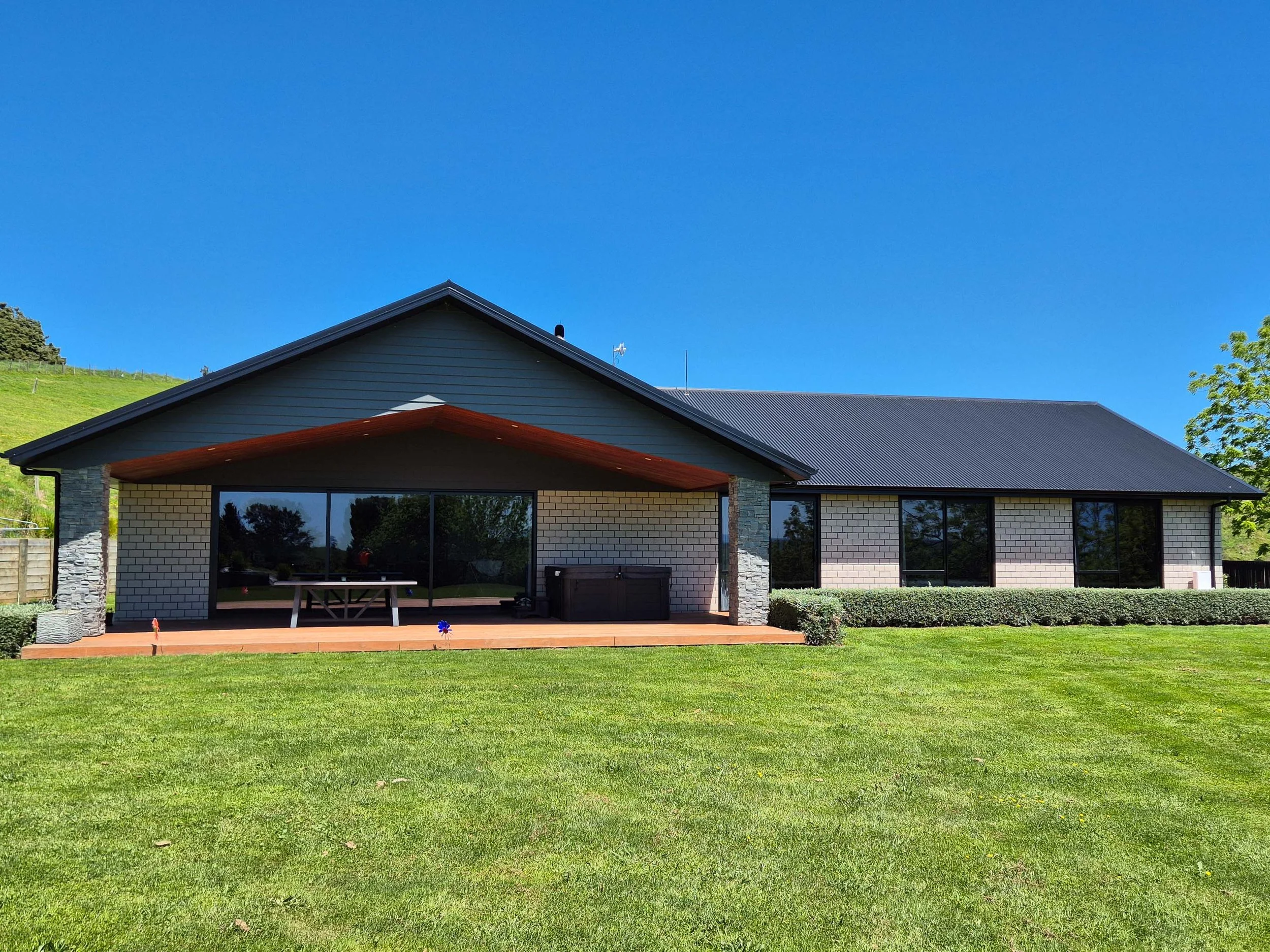 Modern house with a large backyard, a patio, and a lush lawn, under a clear blue sky.
