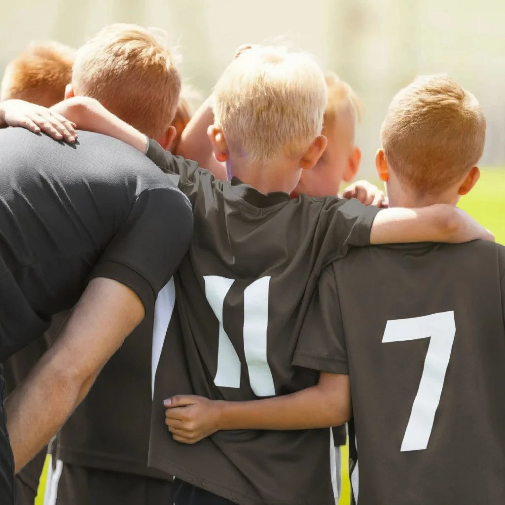 A group of young soccer players in black jerseys with white numbers, huddled together with their arms around each other during a game or practice.