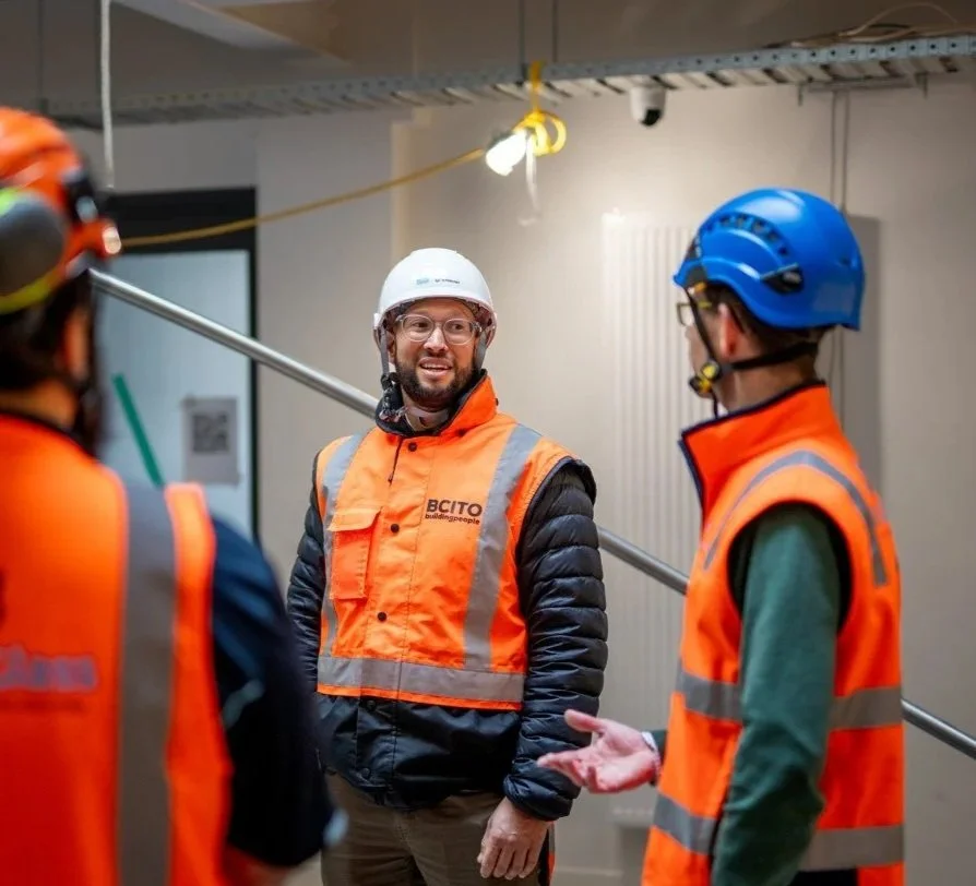 Construction workers wearing safety vests and helmets having a discussion indoors