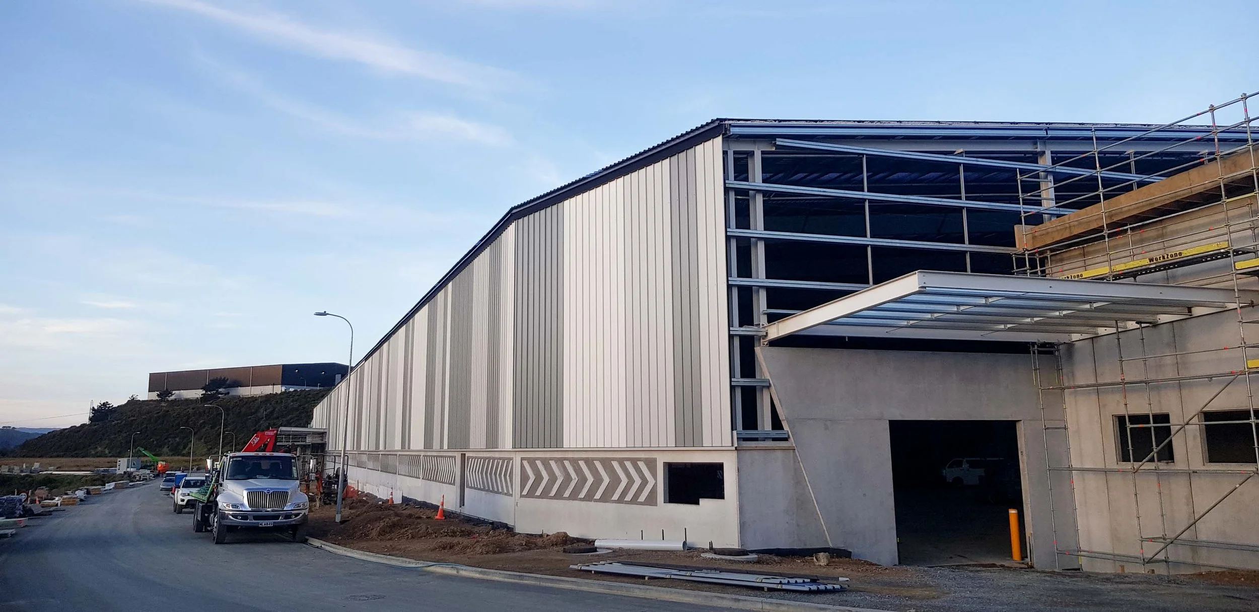 Construction site of a modern building with metal siding, scaffolding, and construction vehicles, during daytime with clear sky.