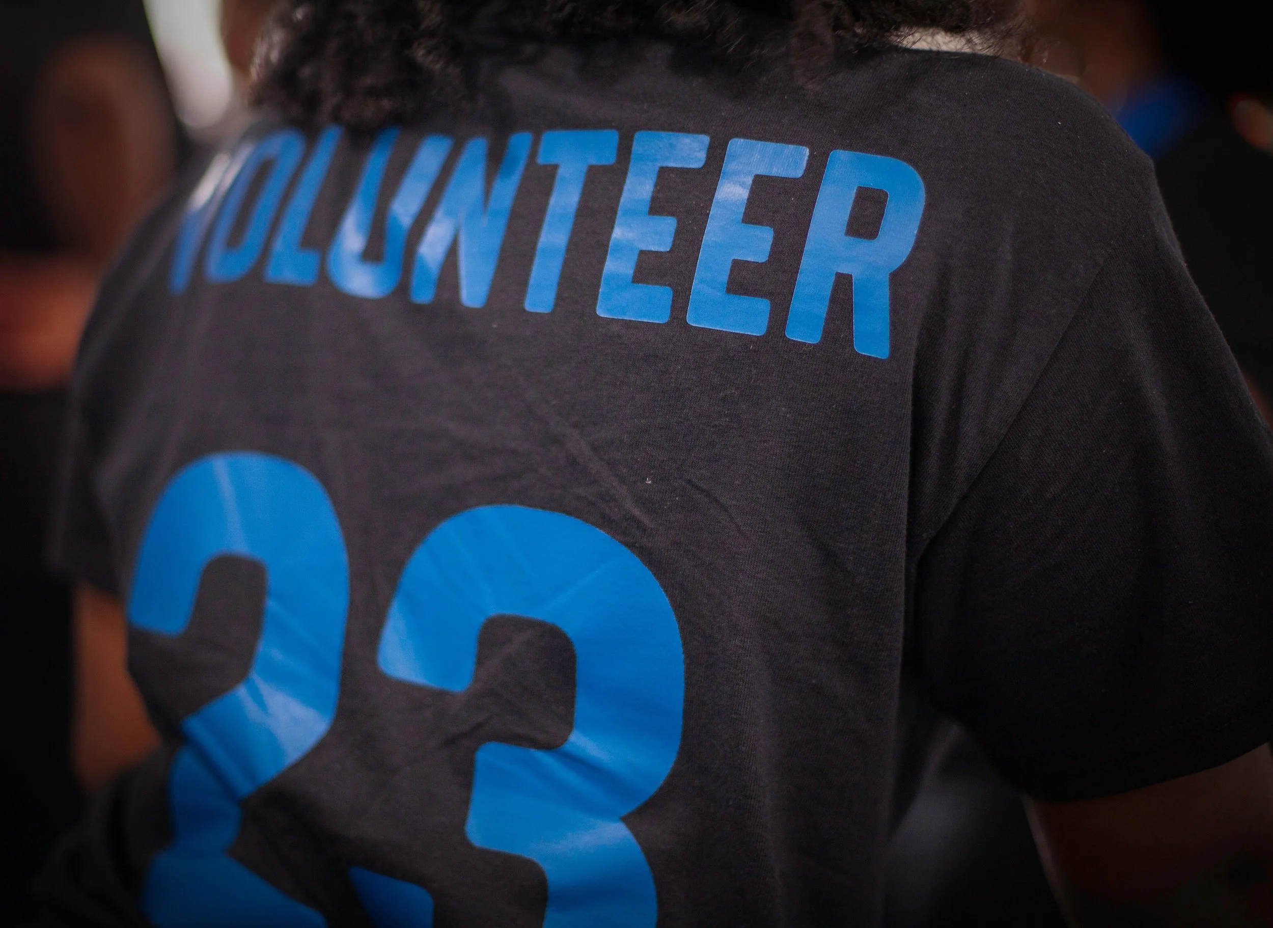 Back of a person wearing a black shirt with blue text that says 'VOLUNTEER' and the number '23'.