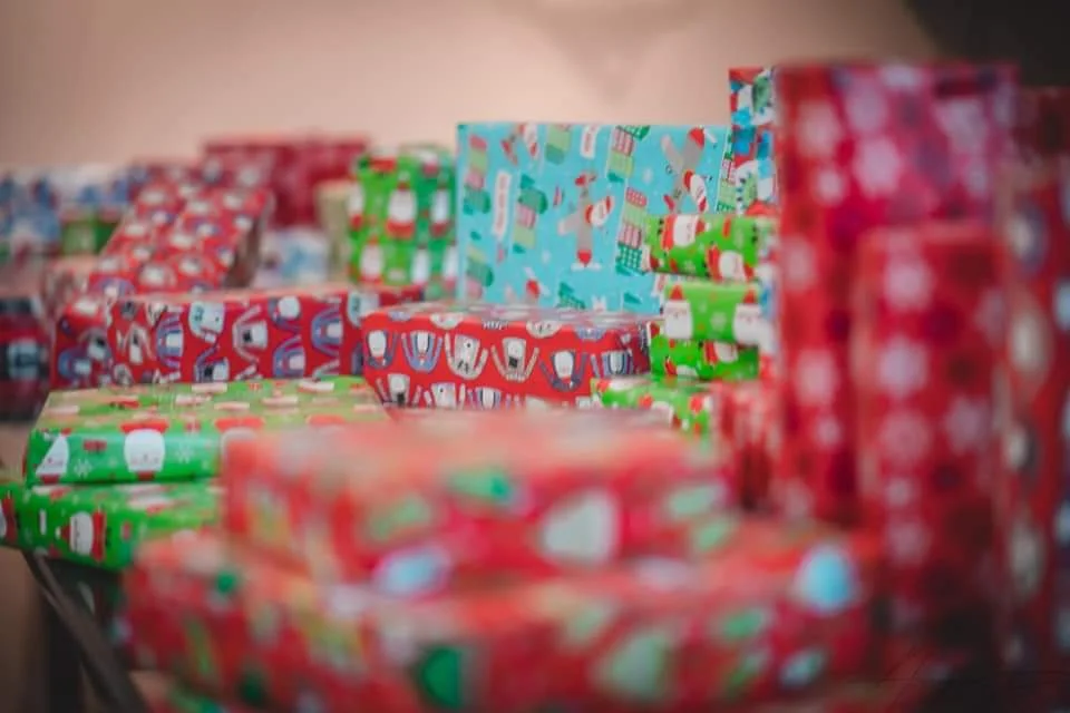 Stacked wrapped Christmas presents with holiday-themed paper featuring Santa Claus, snowmen, and Christmas trees.