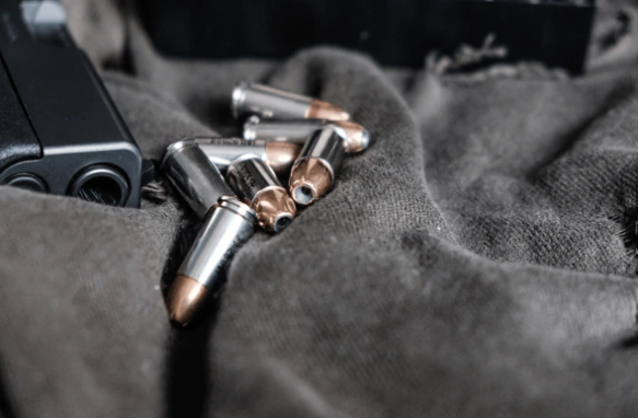A few bullets on dark fabric with a black handgun partially visible.