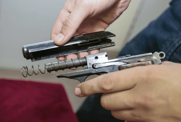 A person holding a disassembled handgun, with the slide, barrel, recoil spring, and frame visible.