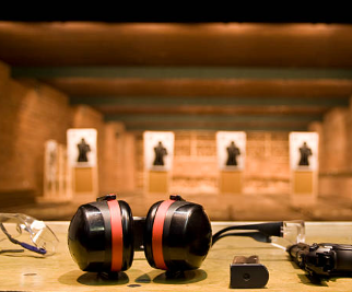 Ear protection headphones and a small camera on a table, with a shooting range in the background featuring targets.