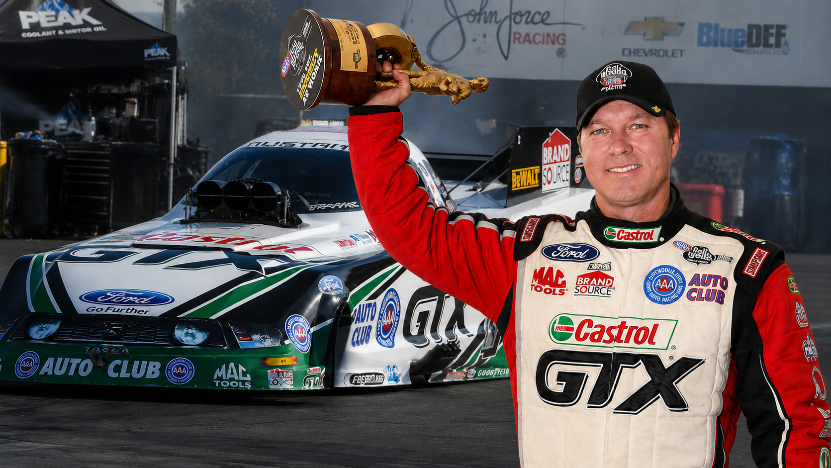 Indy Wrap Works founder celebrating an NHRA win with a championship trophy beside a professionally branded drag racing car.