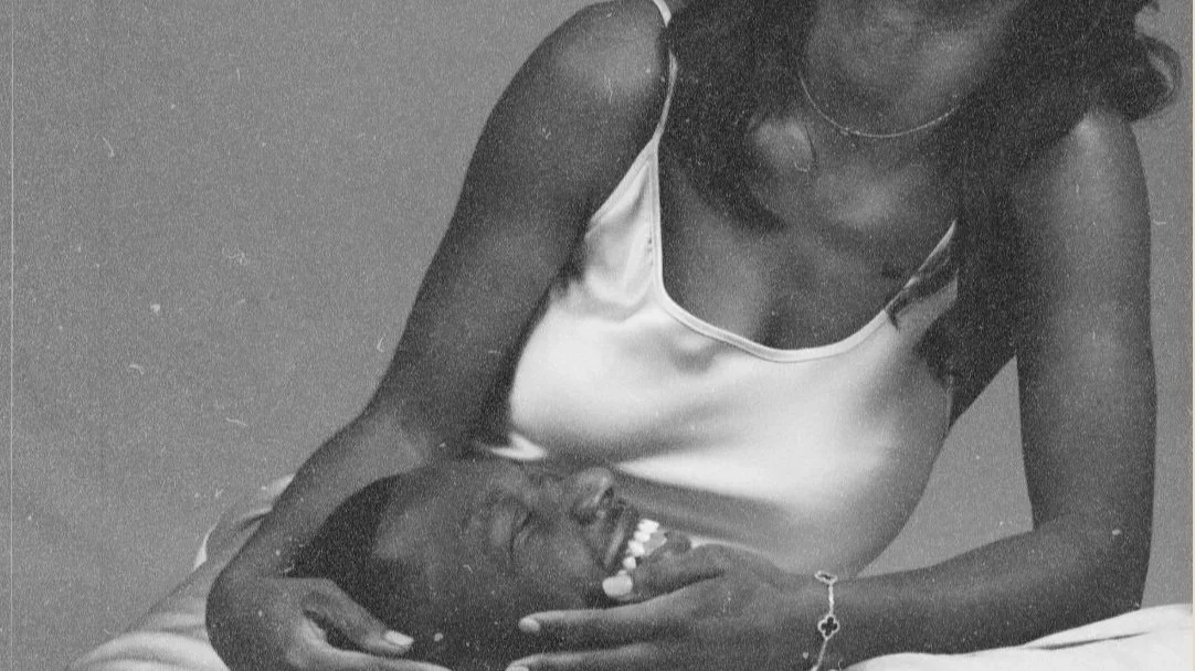 A woman in a satin-slip dress gently touching the chin of a smiling man lying down.