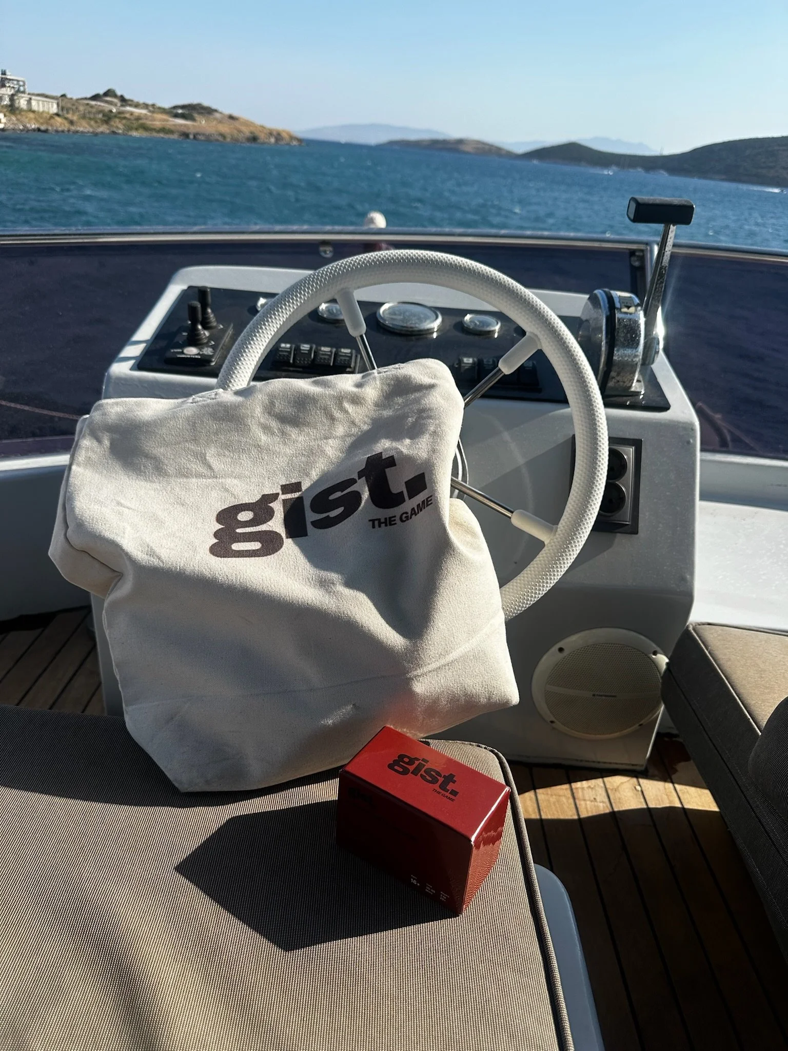 View from the deck of a boat showing the steering wheel, throttle, and navigation controls with a distant landscape of water and islands in the background.