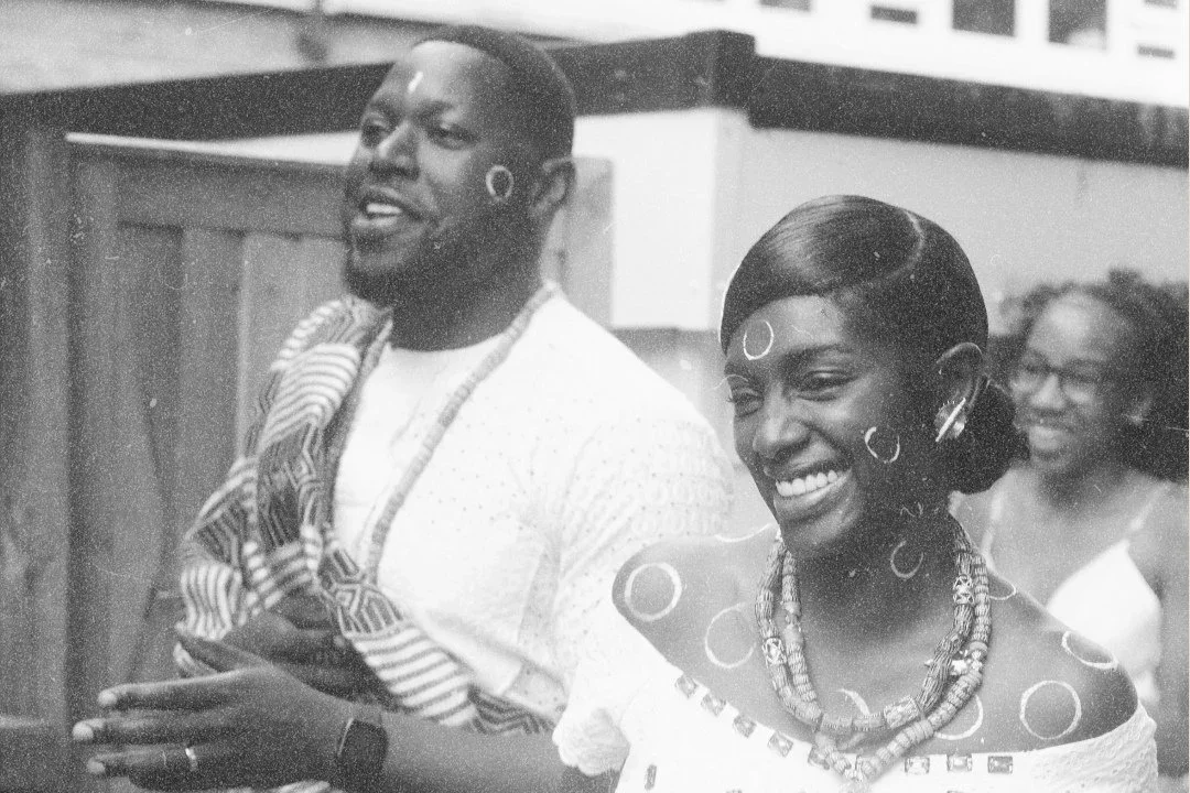 Three people, two women and one man, smiling and engaging with each other in a social setting, with wooden furniture in the background.