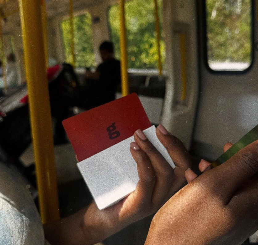 Person holding a red and white box of game cards inside a bus.
