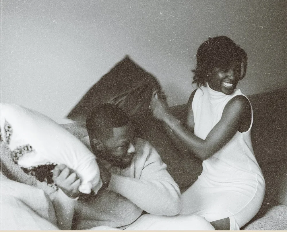 A couple enjoying a playful pillow fight on a bed, smiling and laughing.