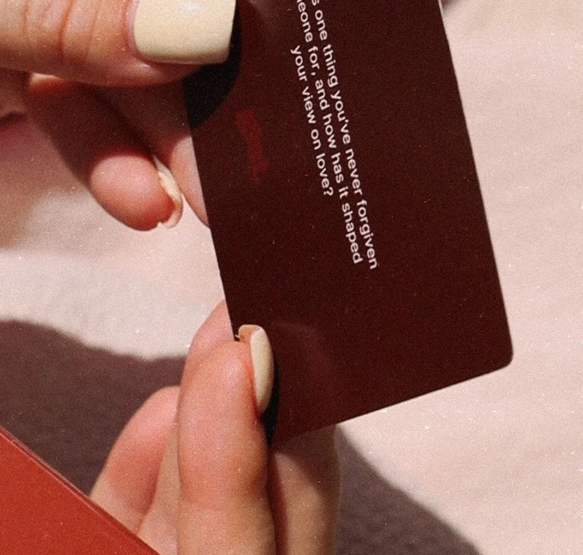 Close-up of a hand holding a red card with white text on it, against a pinkish background.