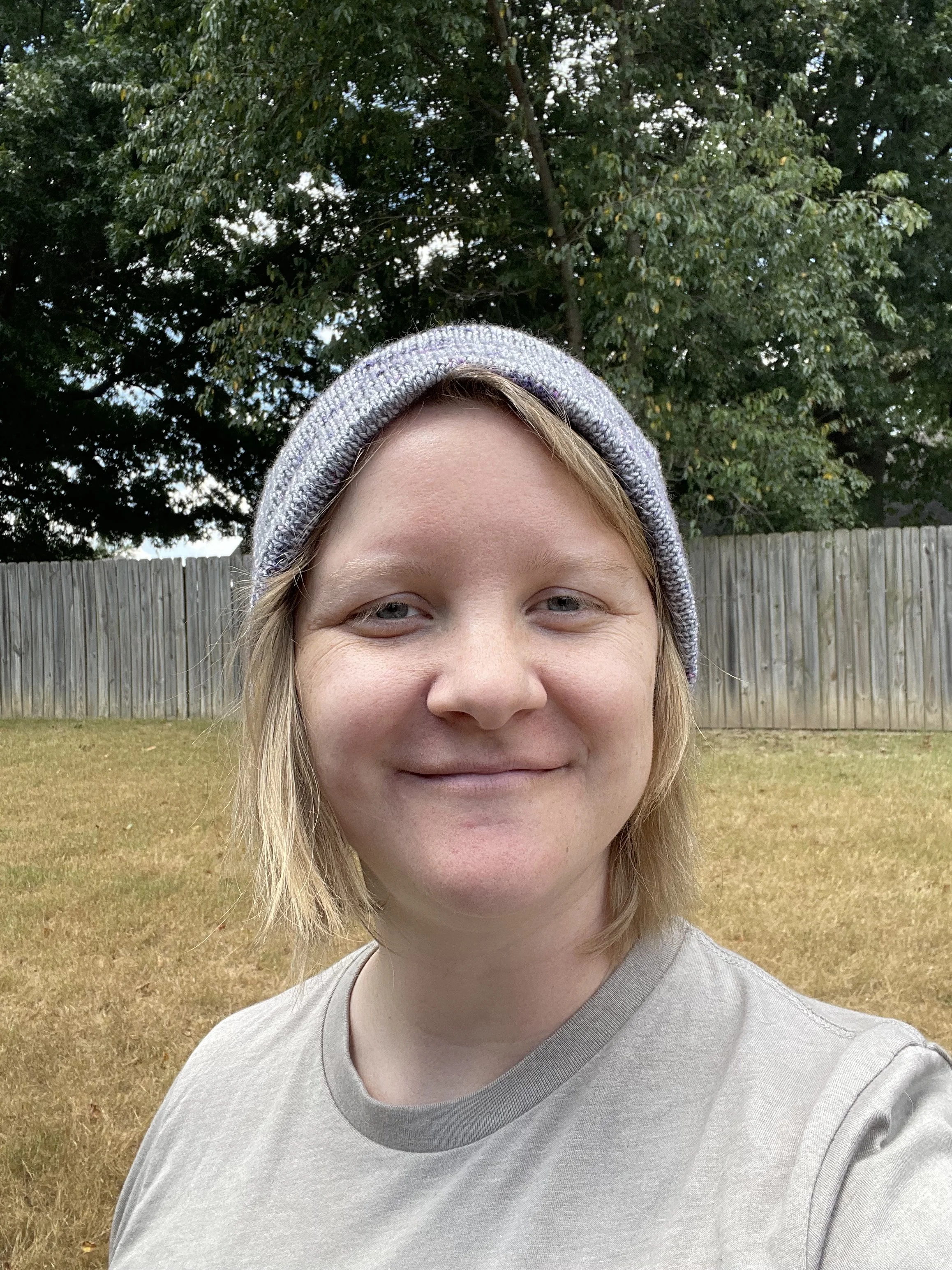 A smiling photo of Hailey, the editor, standing outside wearing a light blue beanie. She has light white skin and short blond hair.