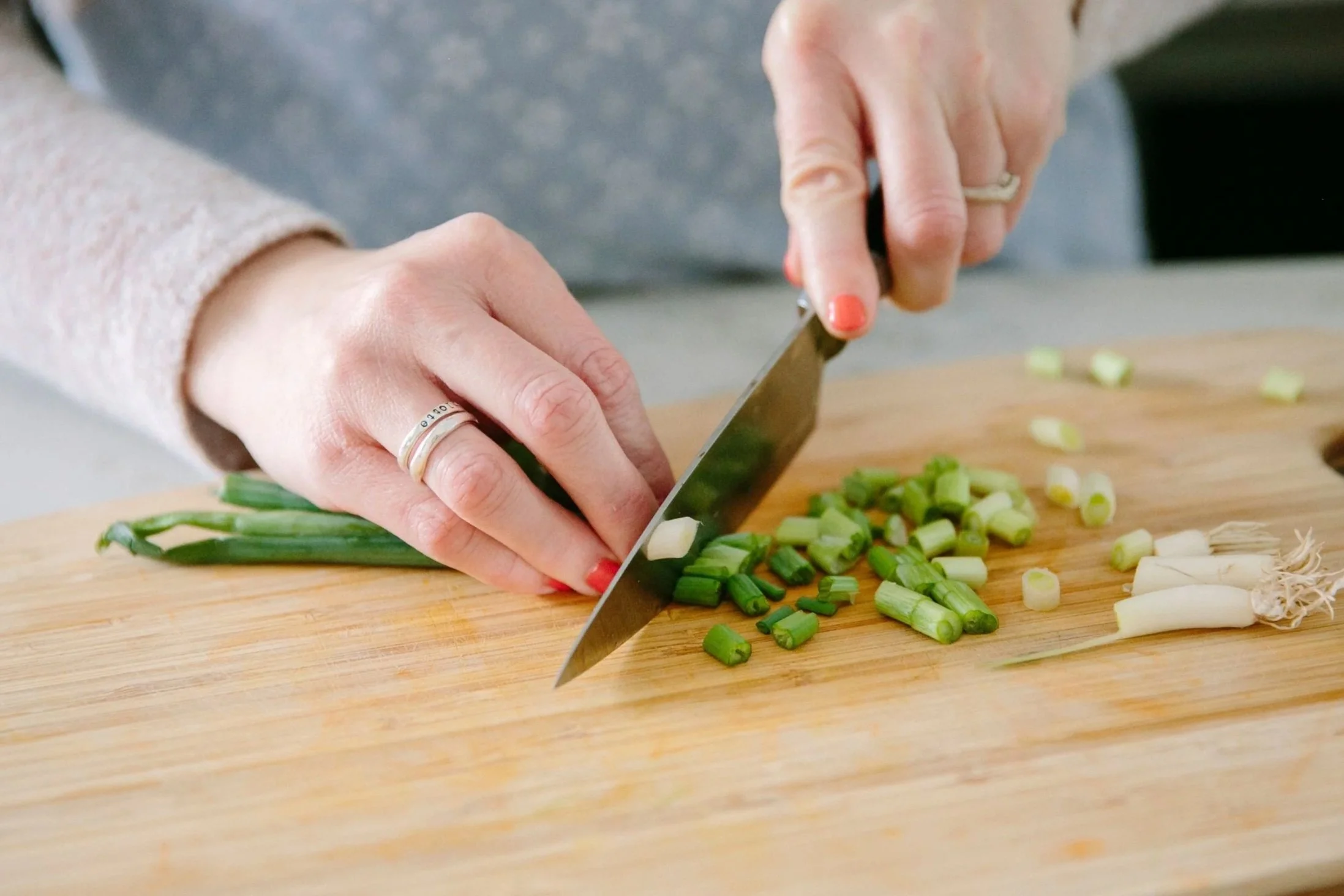 Person chopping green onions on a wooden cutting board.