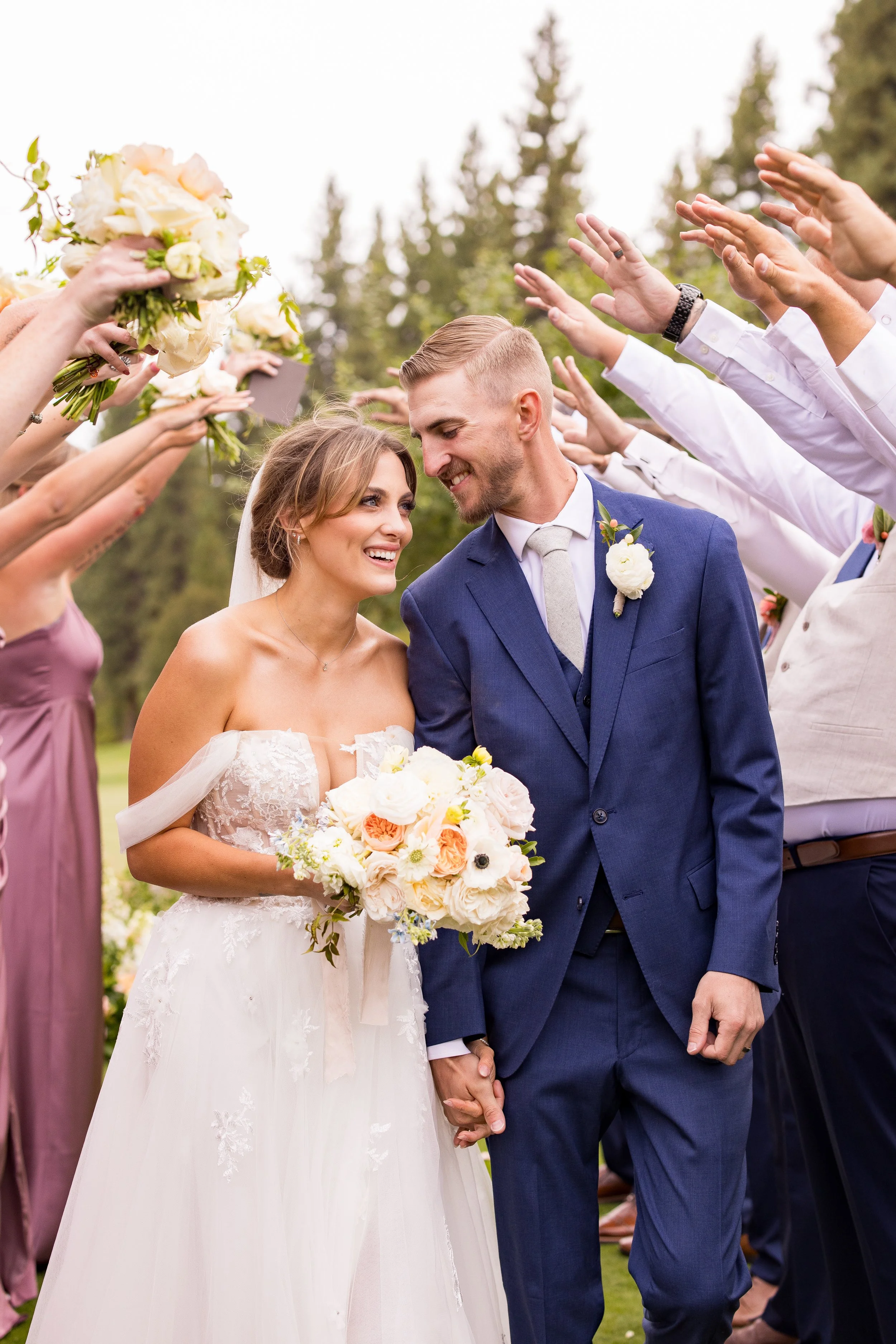 Bride and groom smiling while walking through guests during an outdoor Northern Nevada wedding ceremony exit, featuring soft pastel florals, natural greenery, and an elegant mountain golf course setting.