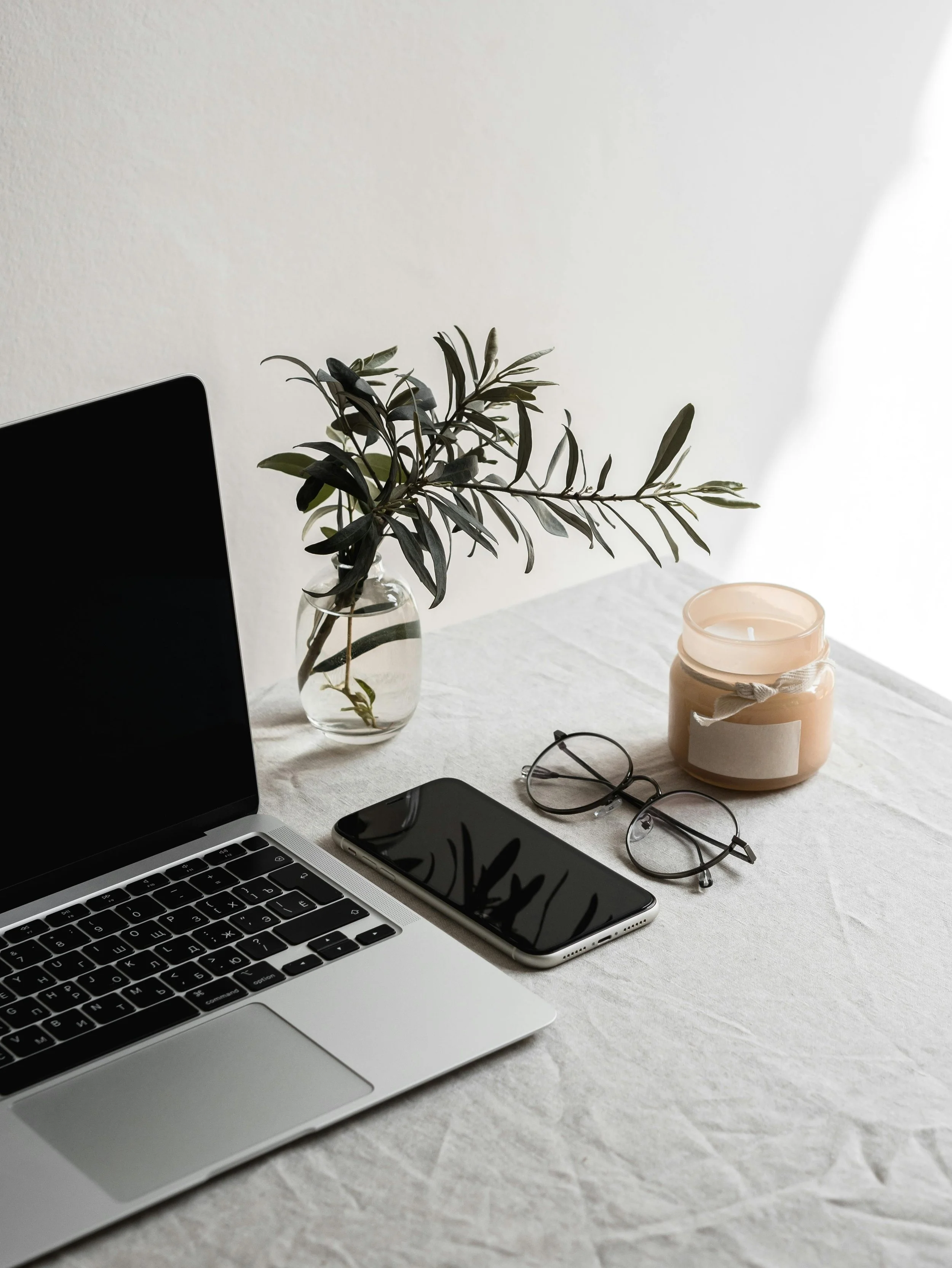 Laptop, smartphone, eyeglasses, candle, and a plant on a white table