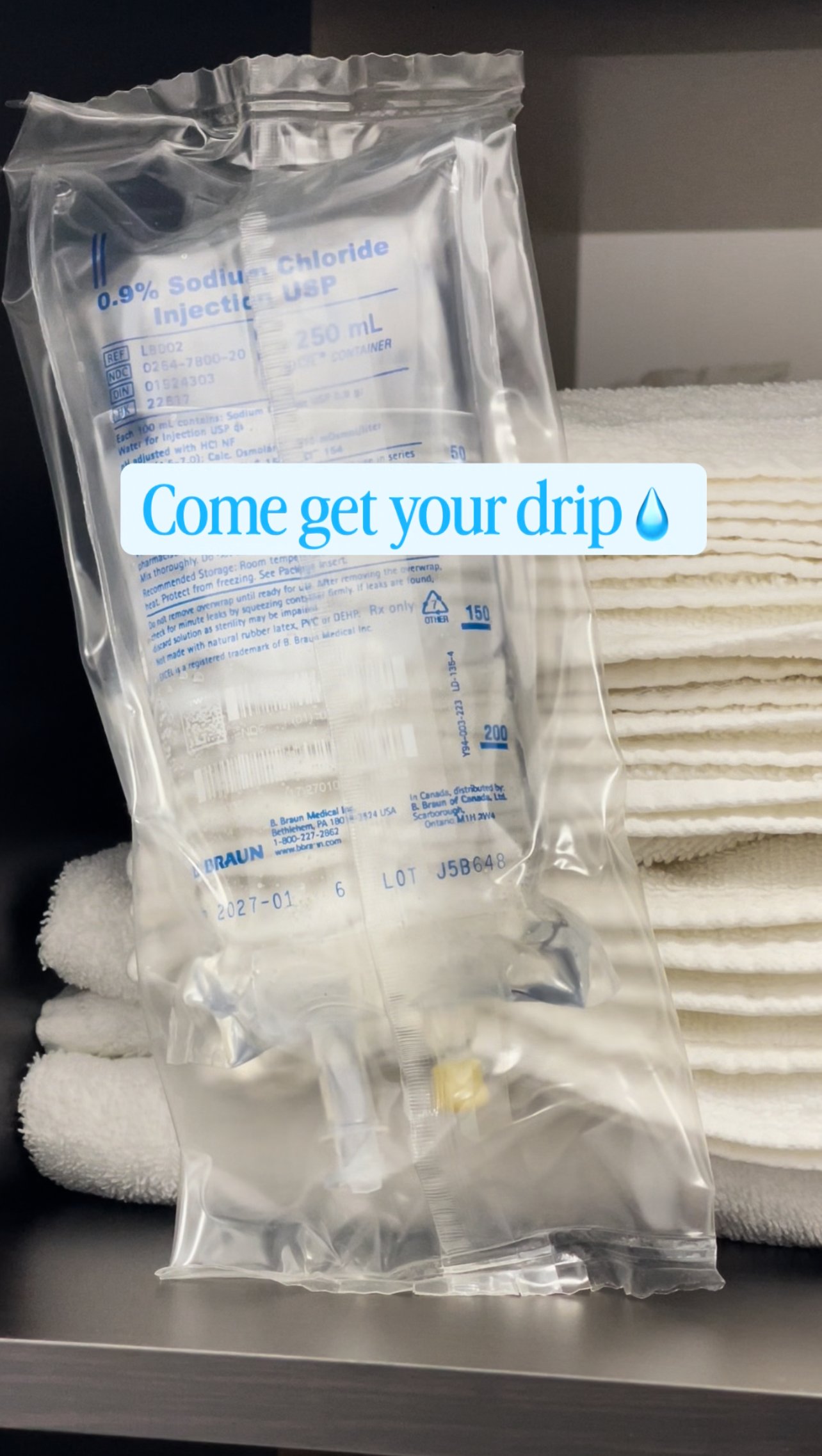 A transparent medical IV bag labeled '0.9% Sodium Chloride Injection USP' with a capacity of 250 mL, placed in front of neatly folded white towels with a blue caption overlay that reads 'Come get your drip' with a water droplet emoji.
