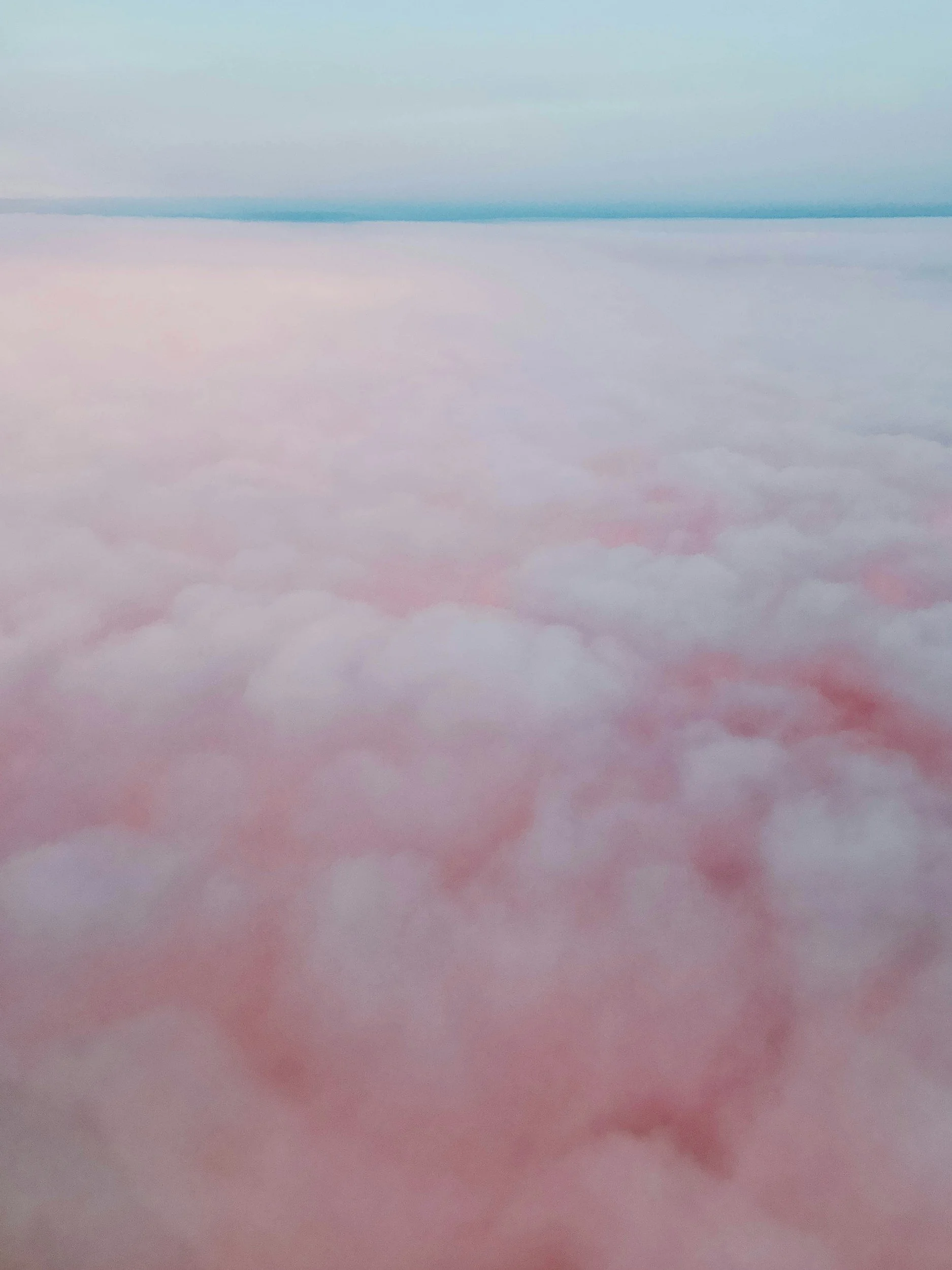 A view from above of clouds with a pastel-colored sky, featuring pink and blue hues.