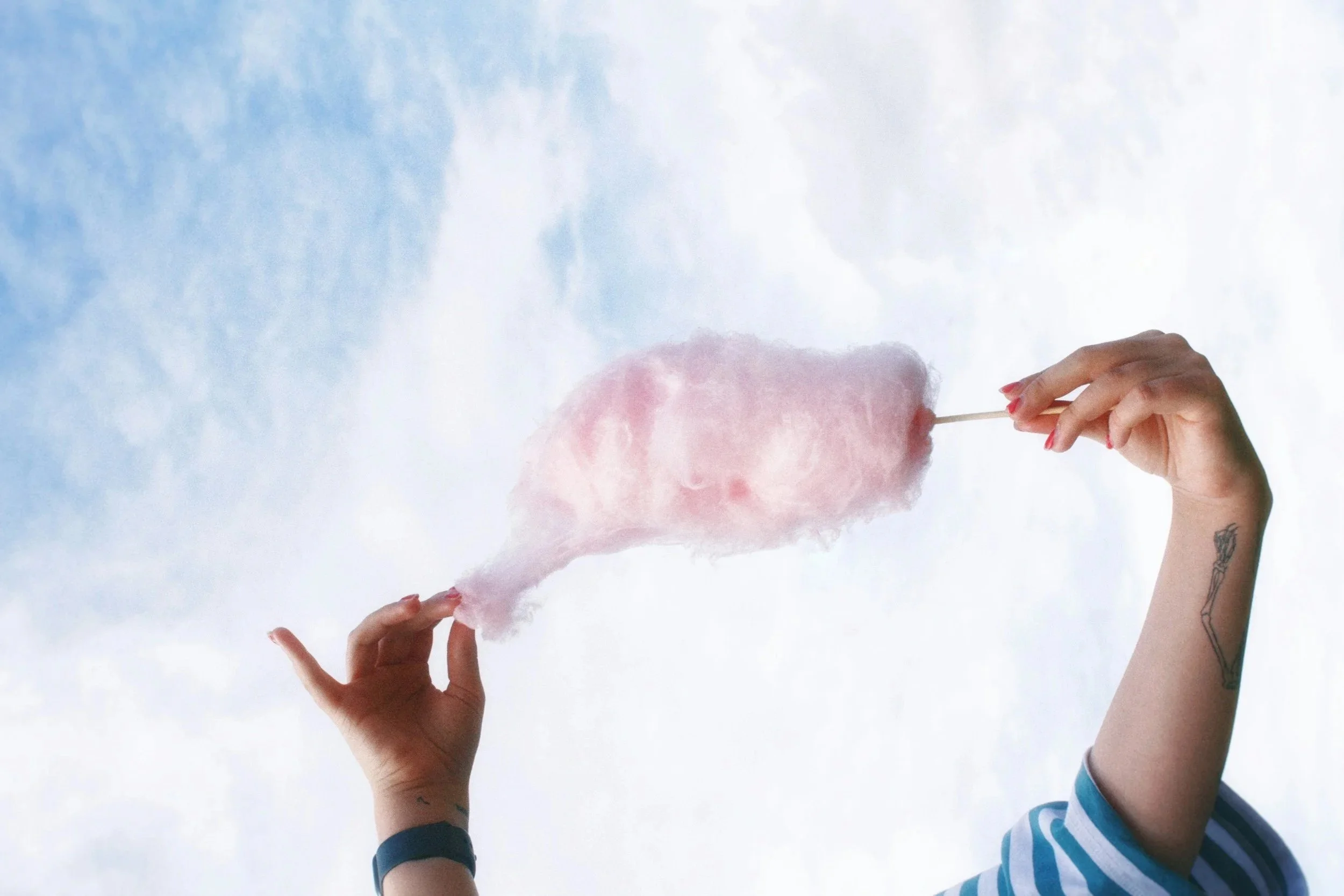 Person holding a pink cotton candy against a cloudy sky