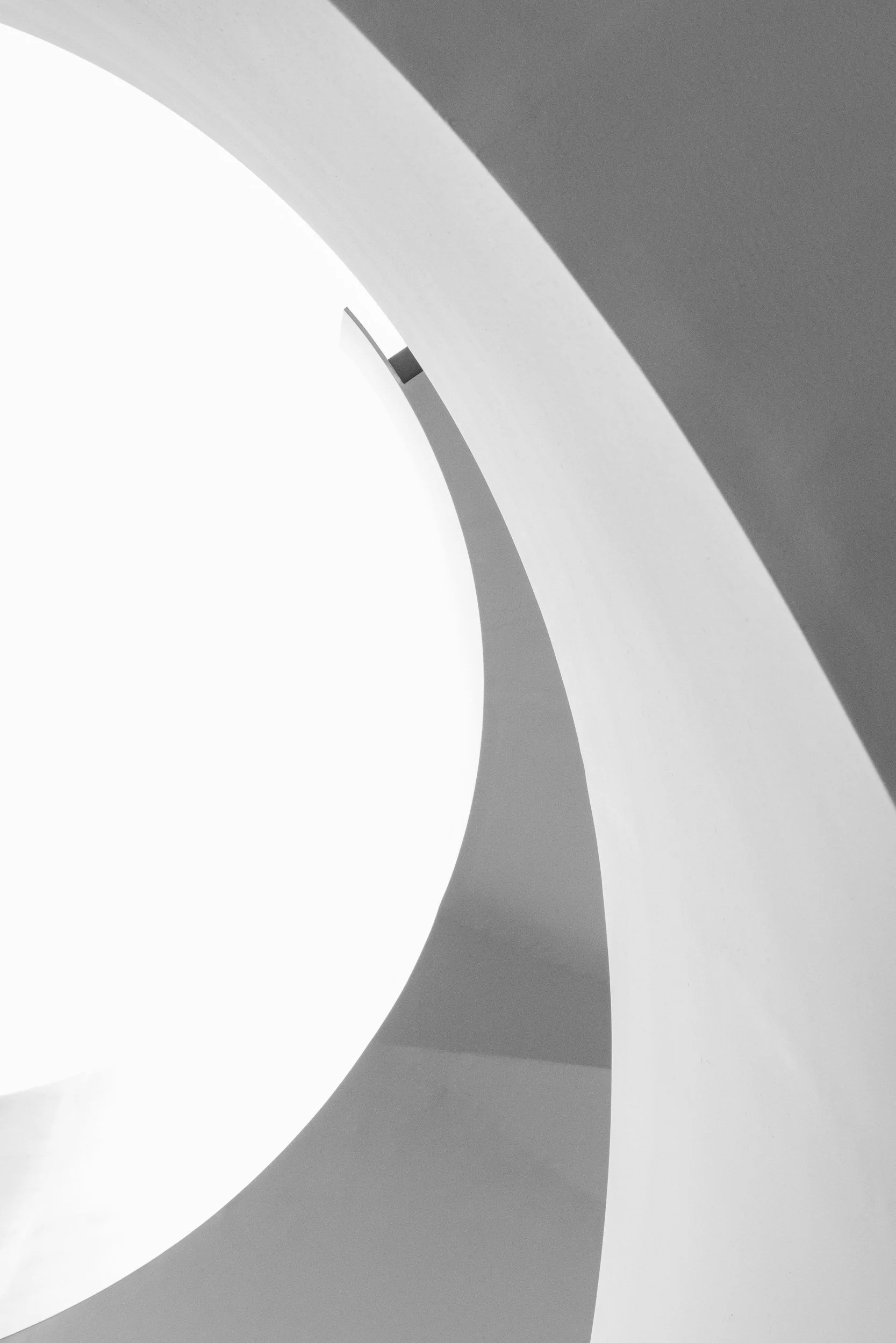Close-up of a modern, curved, white architectural structure with circular openings and contrasting shadows.