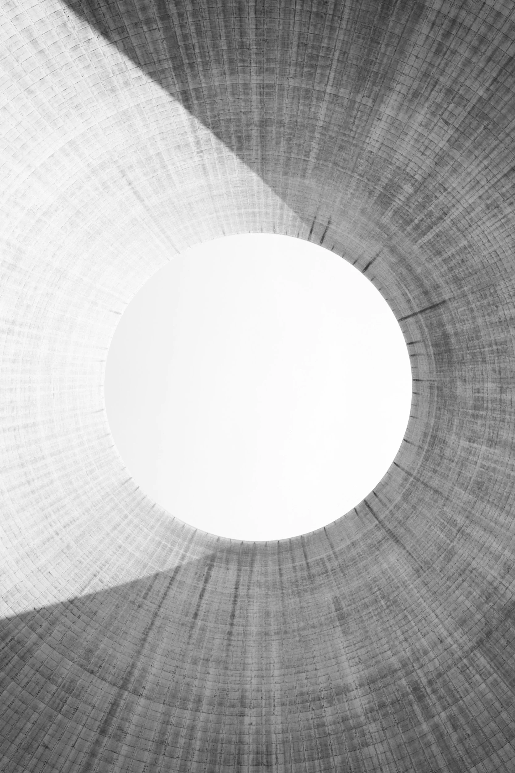 View looking up inside a large concrete cooling tower with a circular opening at the top, showing the textured surface of the tower walls.