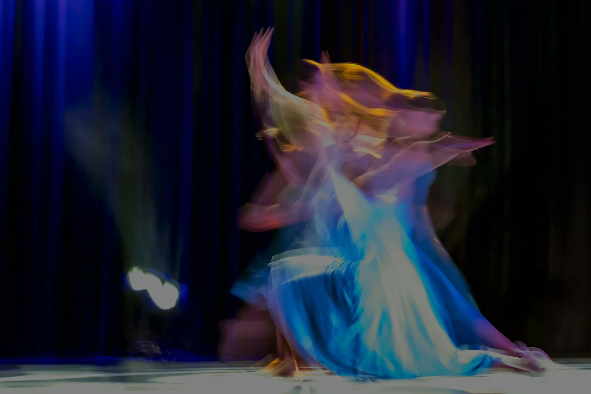Bailarinas en movimiento con trajes coloridos en el escenario, creando efectos de movimiento borroso.