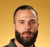 Close-up of a man with a beard and short hair against a yellow background.