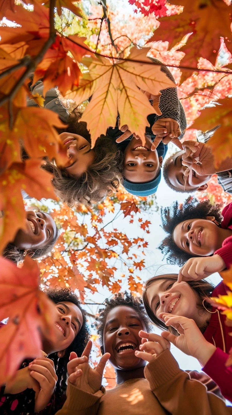 Group of children standing in a circle, looking down at the camera, surrounded by colorful autumn leaves, smiling and making playful gestures.