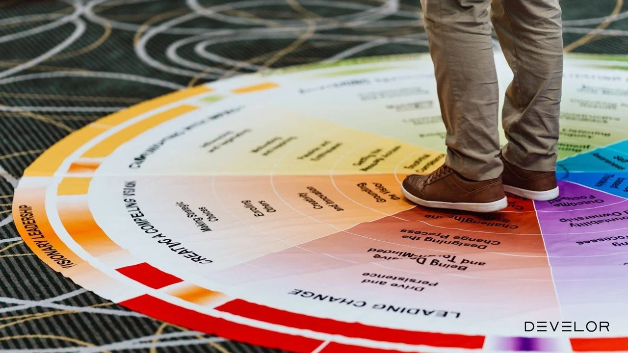 A person standing on a colorful leaflet or chart related to educational or developmental topics, with only their legs visible, on a dark surface with a pattern.